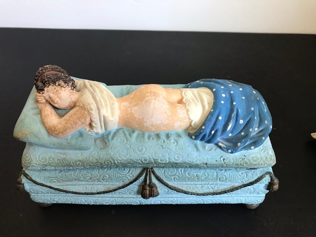 A fun and amusing ceramic box with an erotic reveal. Remove her blanket and she is naked underneath. She is laying on her pale blue day bed with gold tassels and feet, propped up on a pillow looking over at the viewer with a knowing glance. Only she