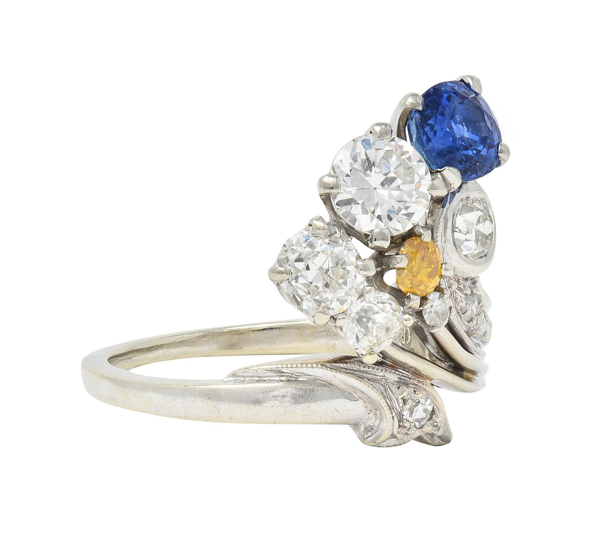 Bypass-style ring terminating with a fanning plume and foliate with clustered sapphires and diamonds
Sapphires are round cut and weigh approximately 0.82 carat total - prong set
One is transparent medium bright blue, and the other is medium yellow