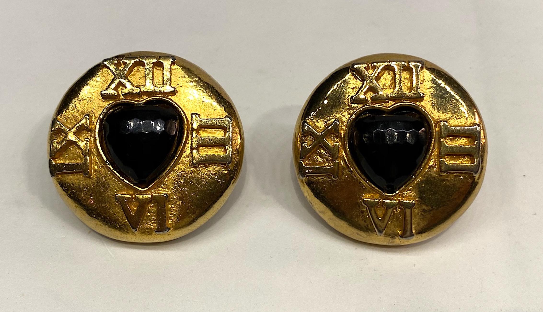 A large pair of 1980s Escada button earrings with heart shape stone. The earrings have a rich 18 carat gold plate and a central faceted black heart shape lucite stone. Surrounding the heart are the Roman numerals of 3, 6, 9 and 12 like a clock. Each