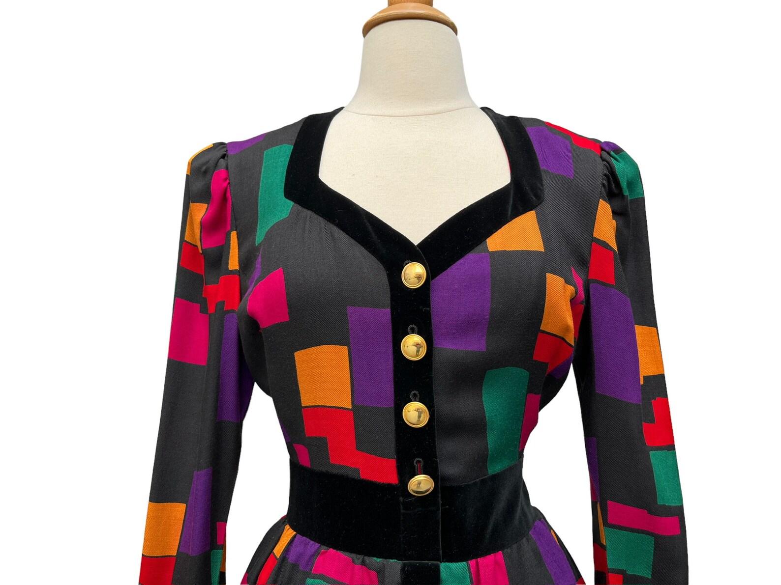 vintage Escada dress. Black wool with a colorful geometric pattern and bllack velvet trim. Gold buttons on the bodice. Peplum waist. Long sleeves with button cuffs. Dress falls to knee length. Back zip closure. Dress is lined, sleeves are