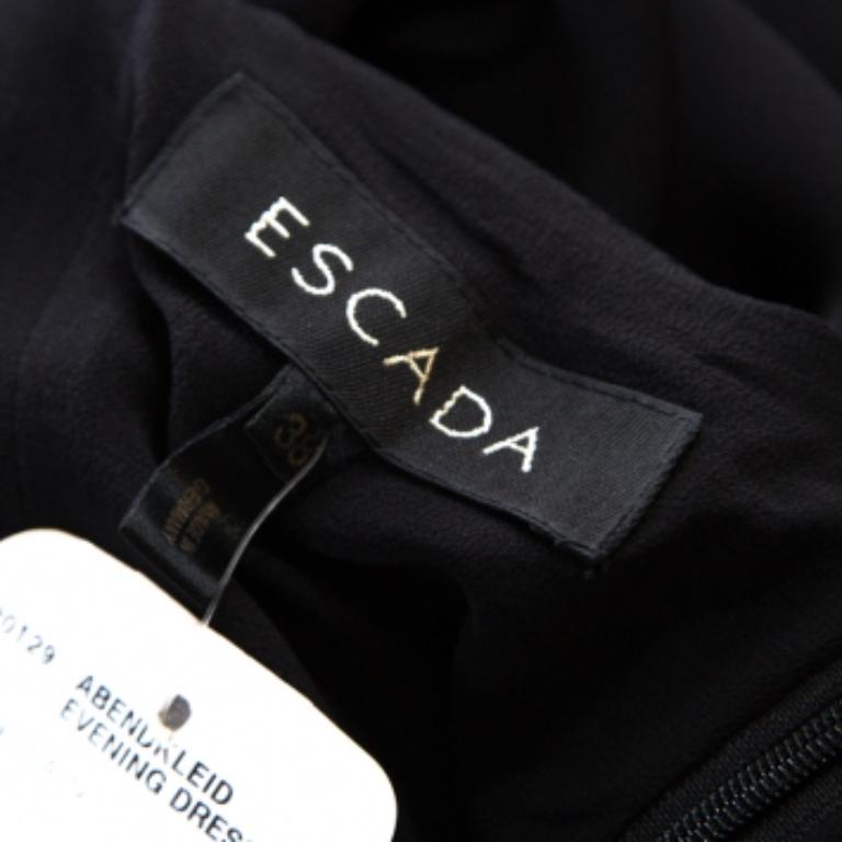  Questo abito da sera di Escada ostenta eleganza con il suo fascino ipnotico e il suo design brillante. Realizzato in seta nera liscia, presenta bellissimi abbellimenti sulla favolosa scollatura e sul fondo. La creazione ha un'ottima vestibilità e