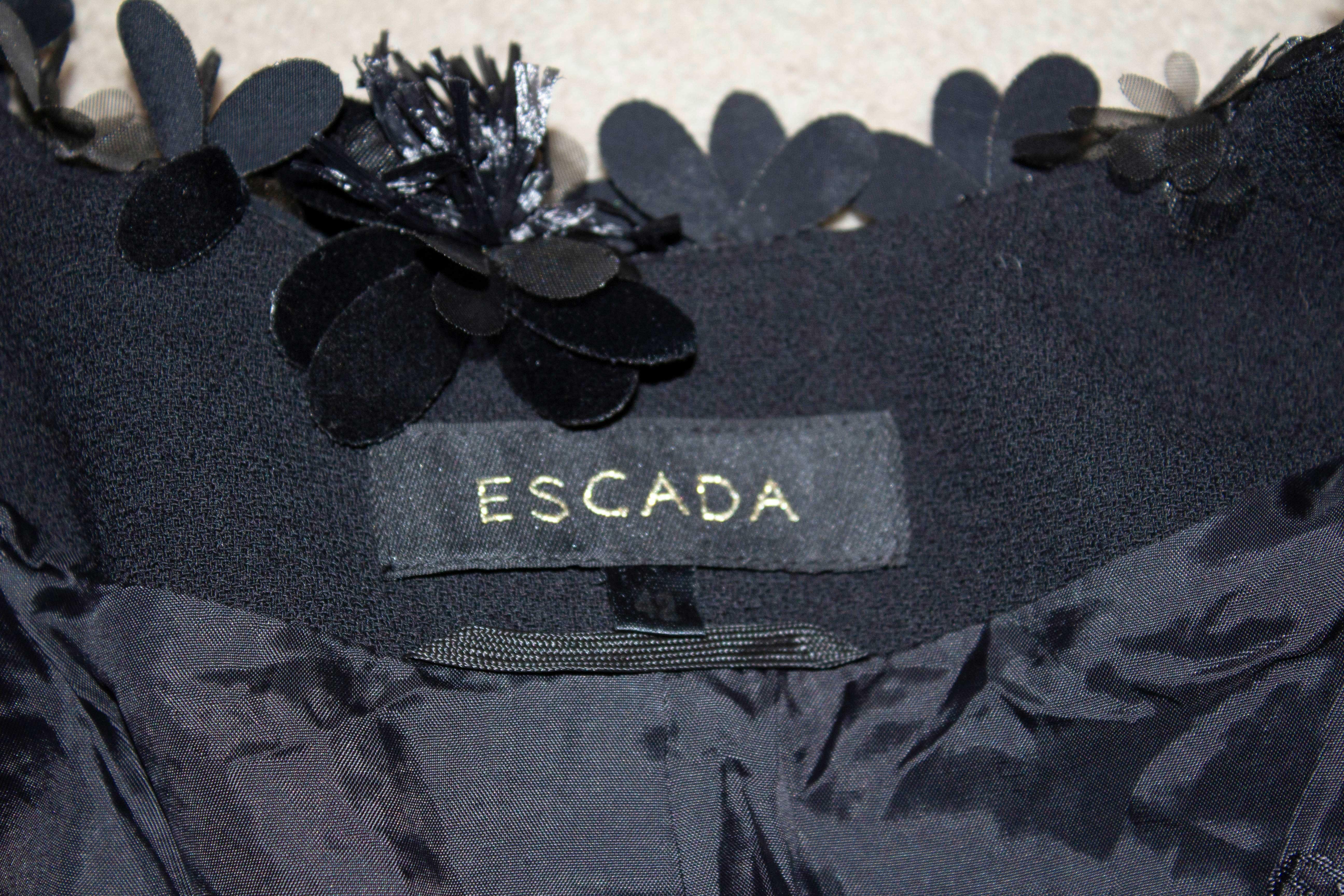 A stunning skirt suit in black wool by Escada. The jacket has a v neckline and fastens with 5 hooks and eyes, and is edged with a floral detail. It is fully lined. The  skirt is A line with flower frill detail, and is lined. Both size 42 .