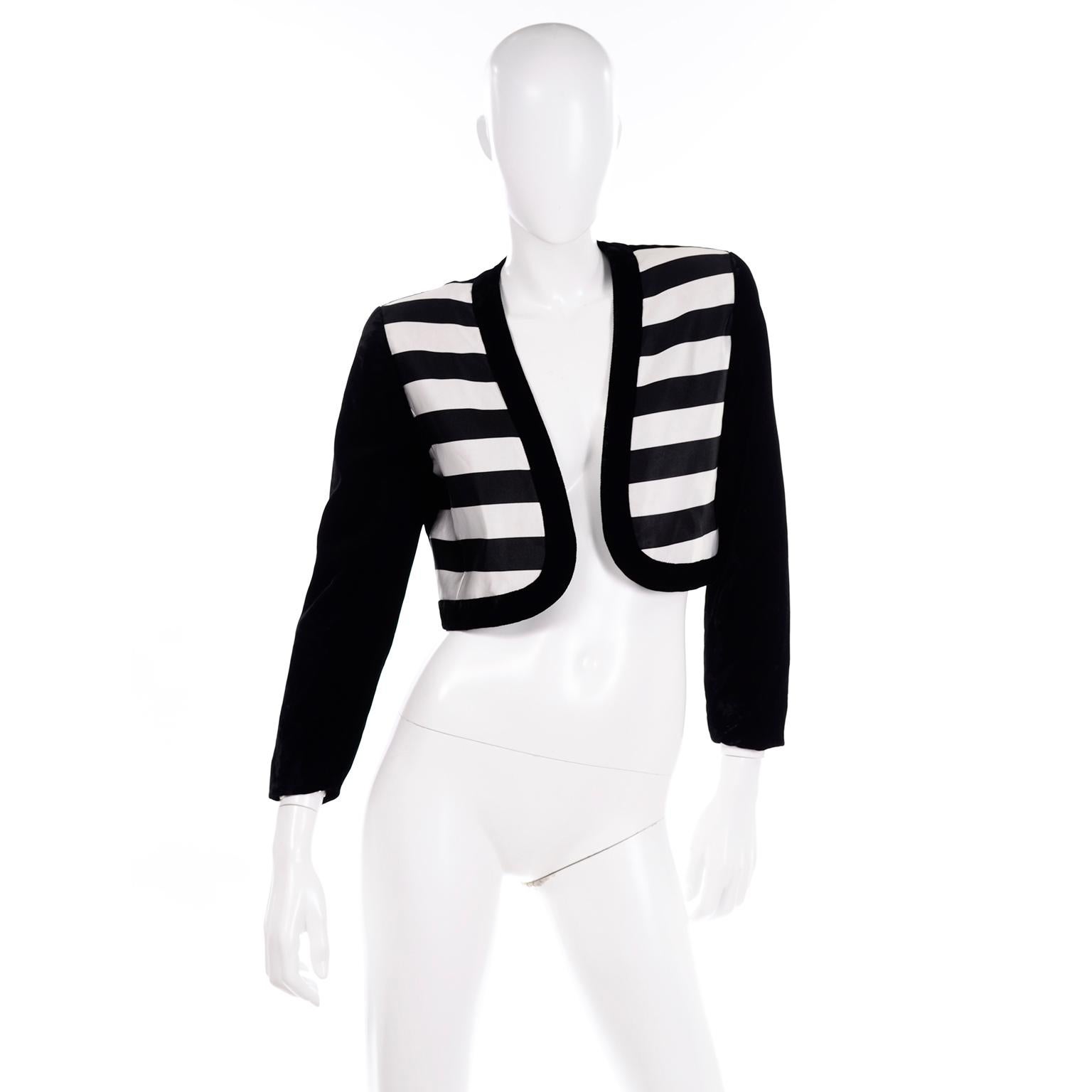 This is a great little vintage evening jacket by Escada Couture. It is black velvet with satin panels in front that form black and white thick horizontal stripes. It is open in front with  no closures, and the hemline curves in front for a very
