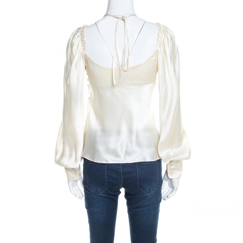 This satin blouse is the essence of a luxurious beauty that will always stay a classic! This flawless creation by Escada features long cuffed sleeves with a center bow tie-up detail. The neckline has a ruffled gathering on the shoulders that