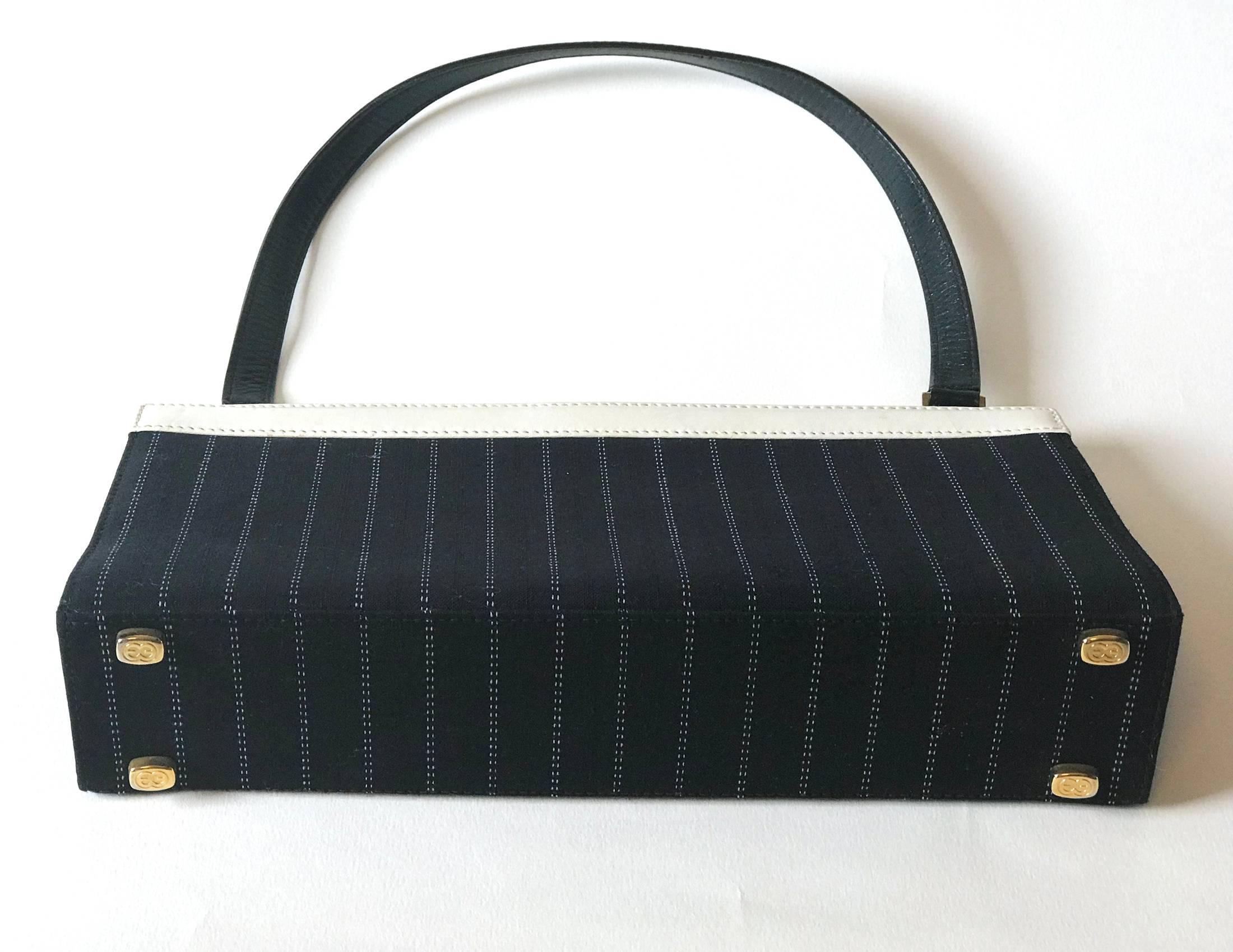 Smart little black and white handbag with golden monogram hardware. Main purse is made of black diplomatic stripe canvas, the opening is white leather  with a gold clasp and handle is in  black leather. Inside is all black with a zip pocket.

The