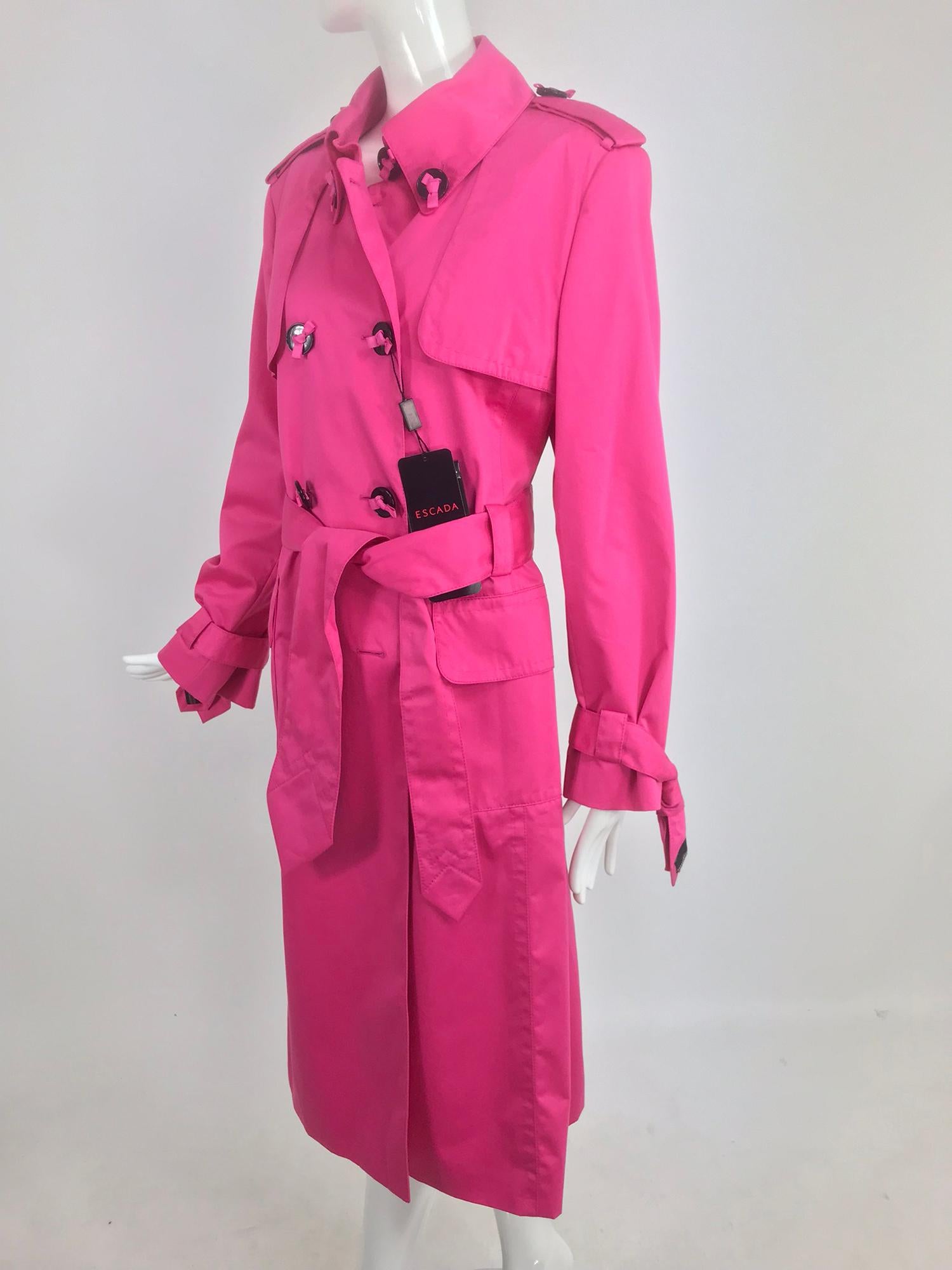 Escada hot pink ribbon Button trench coat NWT size 42. This whimsical coat is perfect to cheer up any rainy day, hot pink poplin fabric in a traditional trench design, double breasted, each button is attached with a tiny black gros grain ribbon bow.