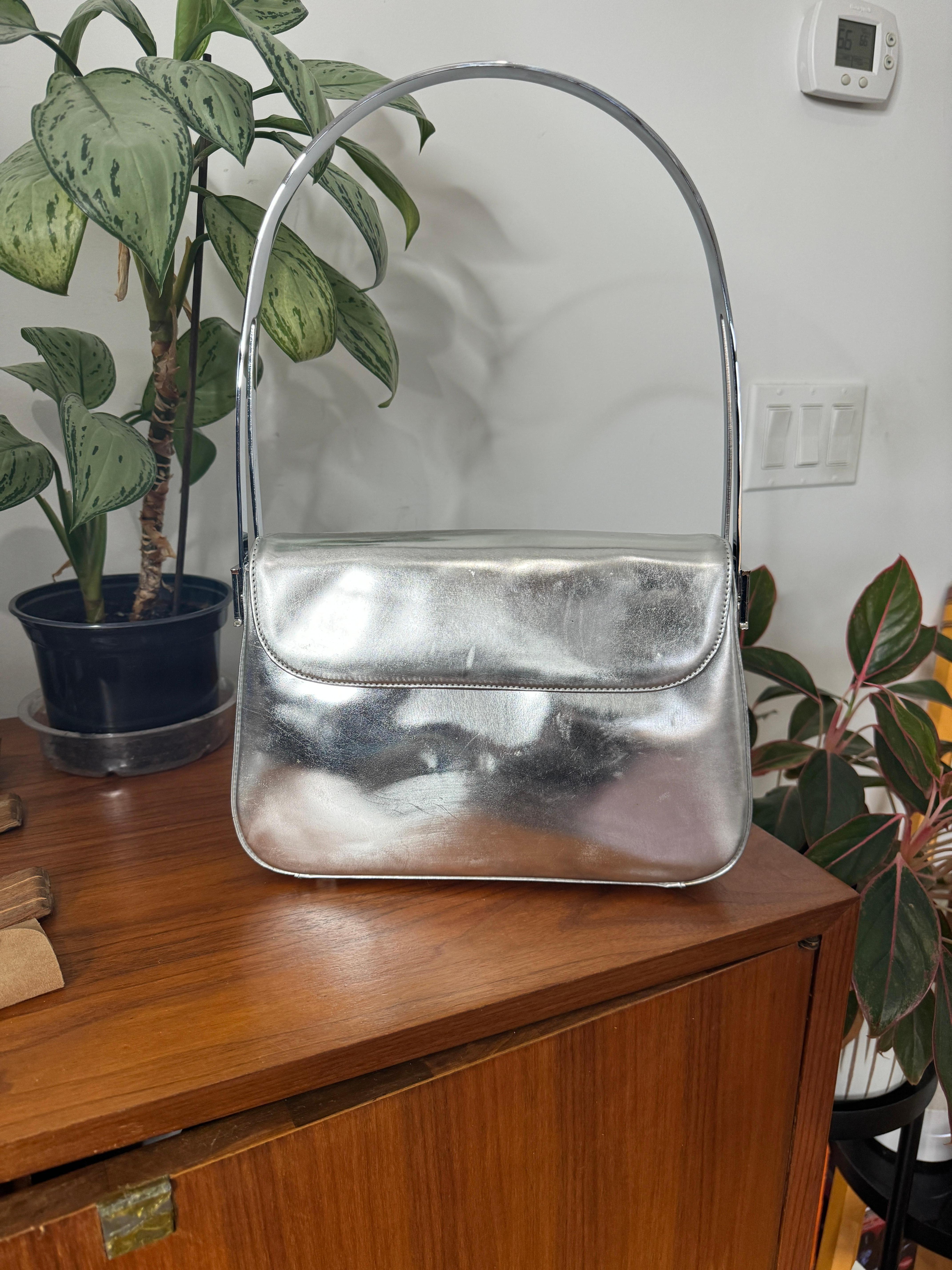 Borsa A. Silver in pelle verniciata di Escada con hardware in tonalità argento. Scomparto interno con cerniera. Misure interne rosse - 15,5 pollici. Maniglia abbassata x 10,5 pollici. W  x 3 pollici di profondità. Ha un'atmosfera da A Space Age.  Si