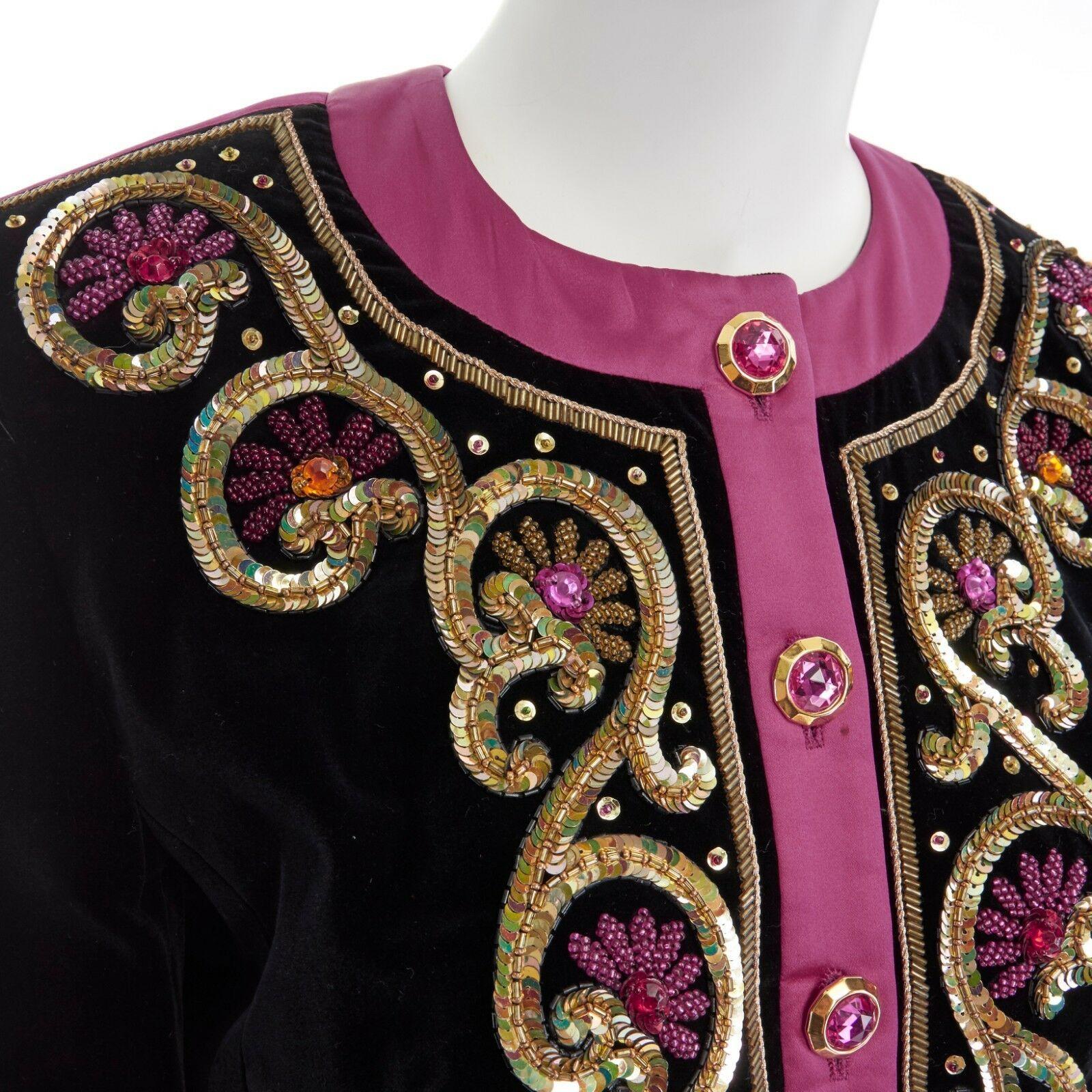 ESCADA MARGARETHA LEY 1980's black velvet gold sequins beaded bolero jacket S
ESCADA BY MARGARETHA LEY
1980's jacket. 
Black velvet. 
Fuschia pink ribbon trimming at collar and along sleeves. 
Round neck. 
Gold-tone pink jewel button front closure.