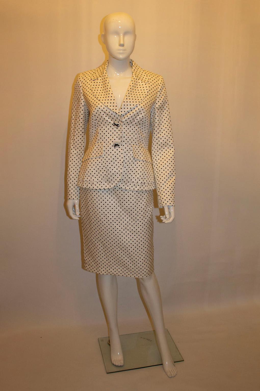 A headturning and fun skirt suit by Escada. In a lovely silk and cotton mix fabric, the outfit has a white background with black spots. The jacket has cut away lapels  and fastens with two decorative popper buttons, and has a pocket on either side.