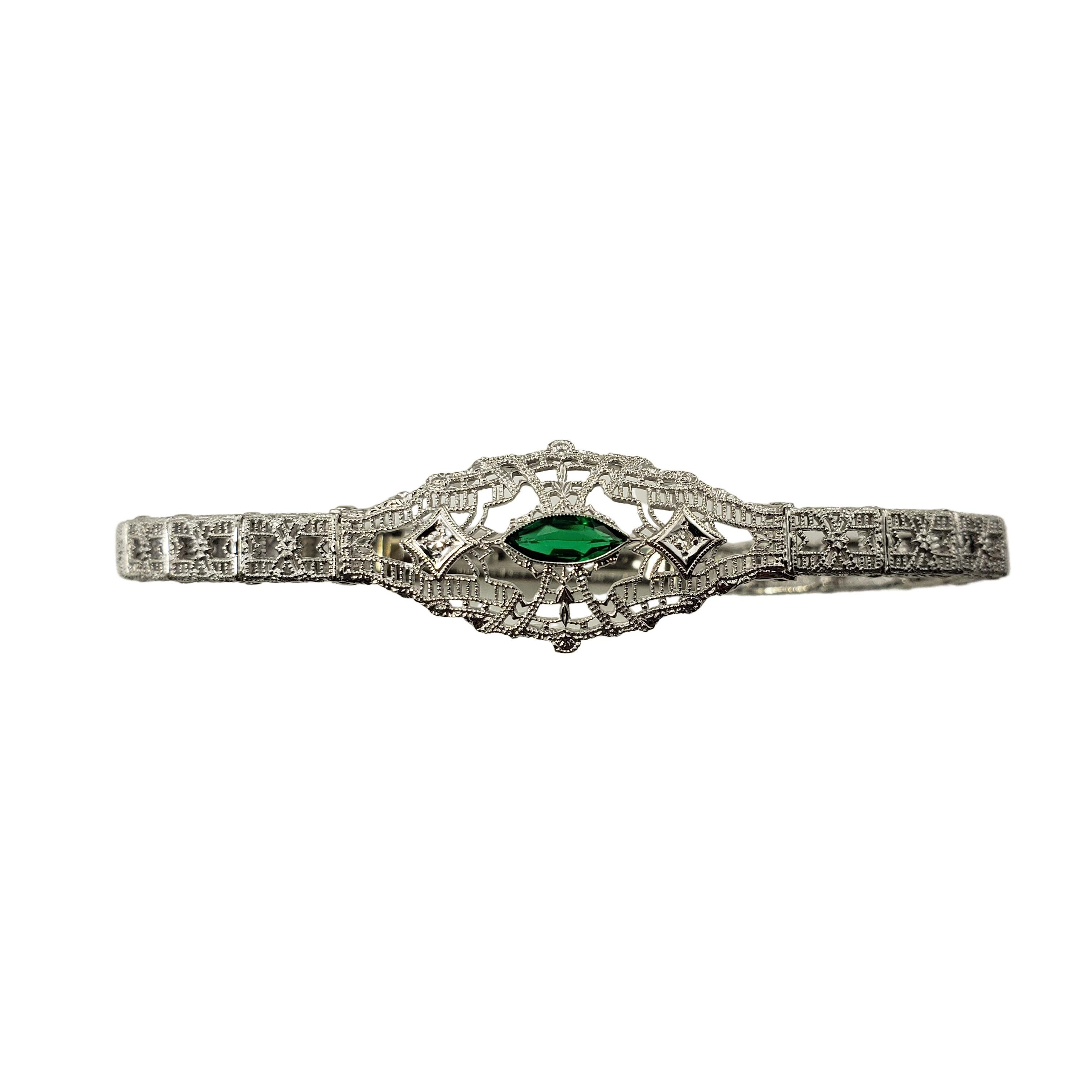 This lovely bracelet features two round single cut diamonds and one simulated marquis emerald set in beautifully detailed 10K white gold filigree. 
Width: 15 mm.

Approximate total diamond weight: .02 ct.

Diamond color: J-K

Diamond clarity:
