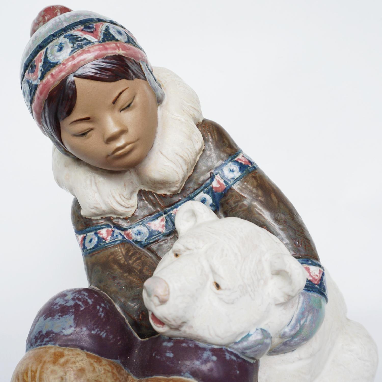 'Inuit Girl Playing' pottery figure sculpted by Juan Huerta for Lladró. First issued in 1978. Depicting a young Inuit girl sitting and playing with a Polar Bear cub. Excellent fine hand painted detail. Numbered 2097.

Dimensions: H 23cm, W 16cm, D