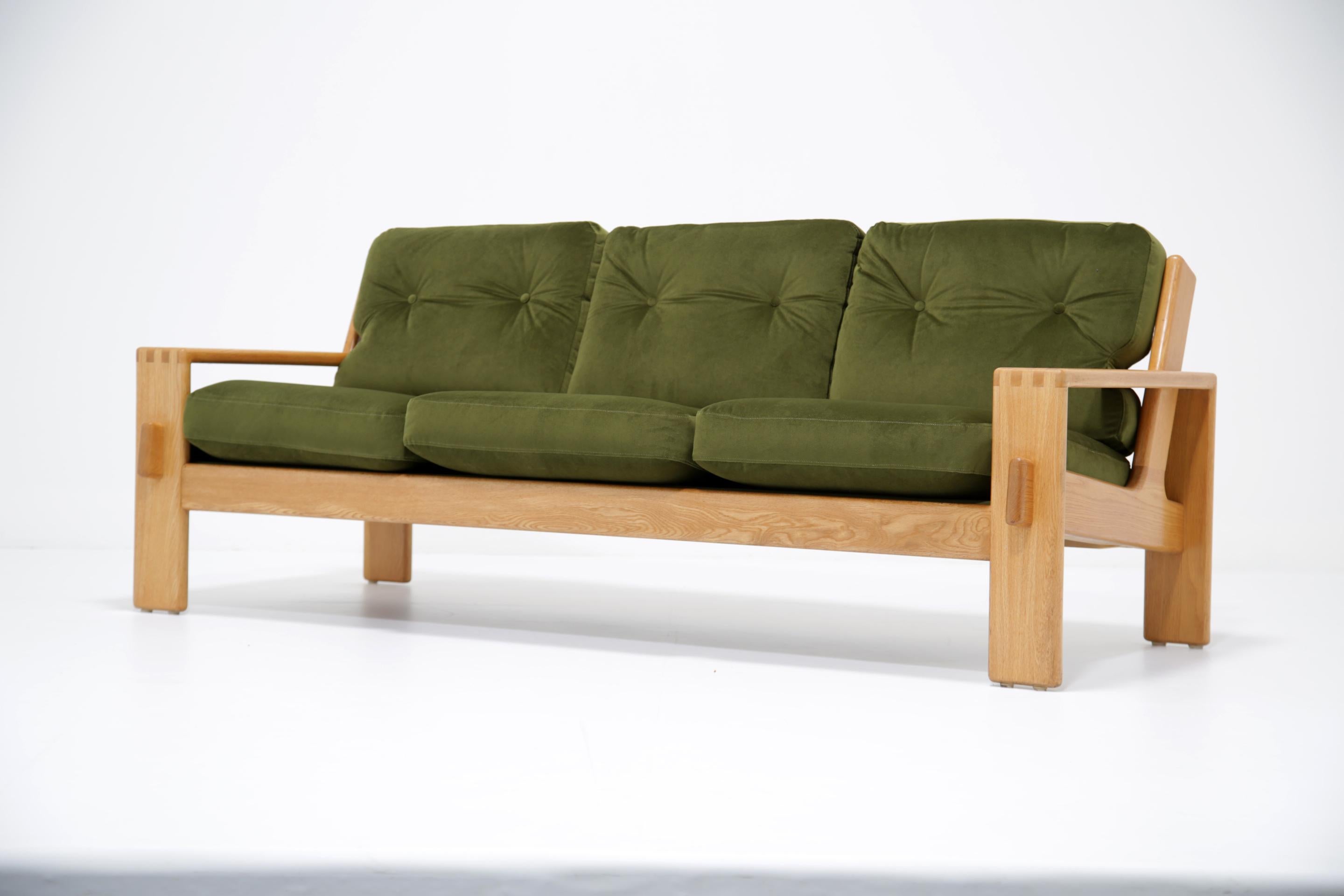 Este magnífico sofá de tres plazas presenta una estructura de roble macizo con brazos anchos de tablón, juntas vistas y bonitos soportes en ángulo que sobresalen en las patas delanteras rectangulares, creando un diseño minimalista único pero