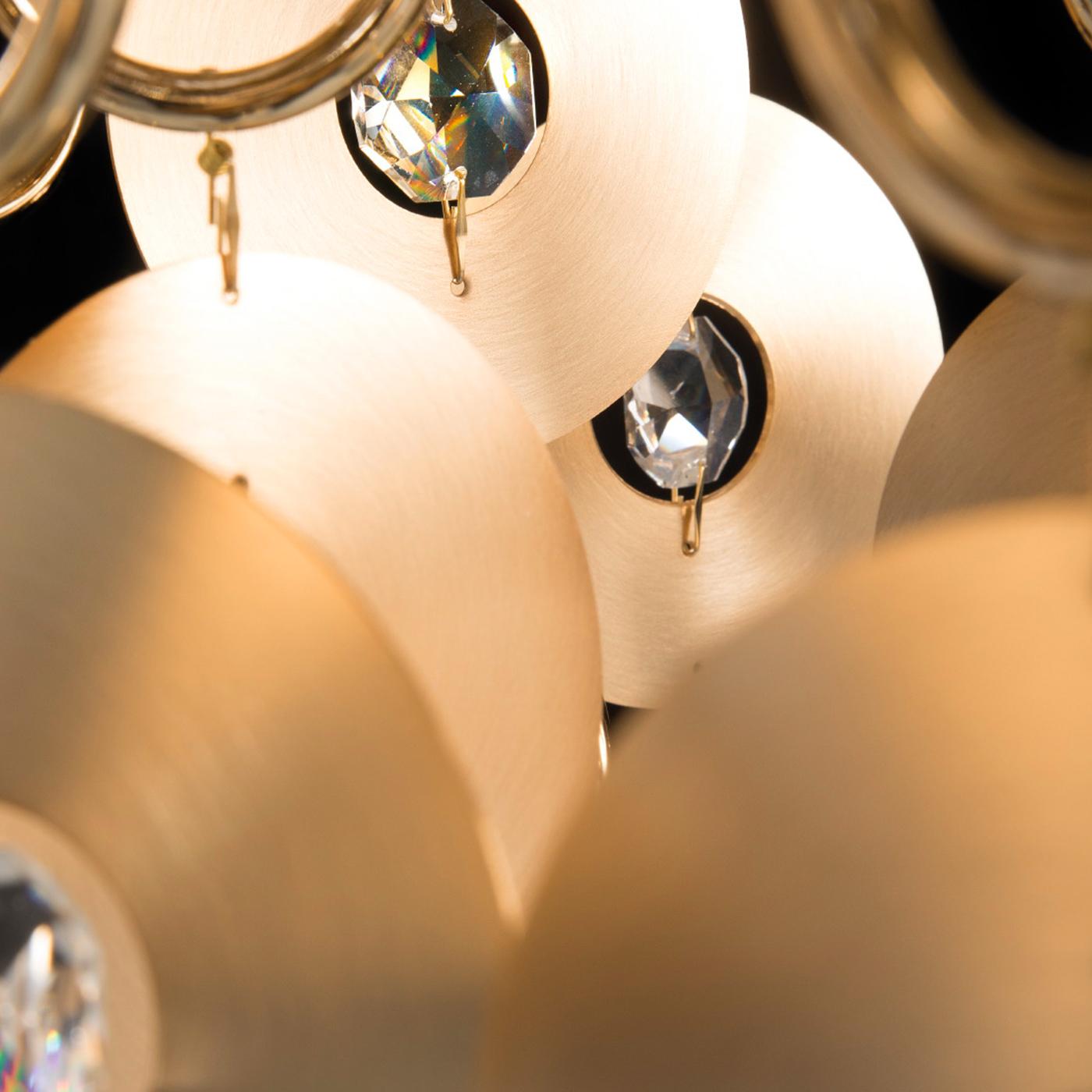 Des disques en laiton satiné entourant un cristal de taille royale et des anneaux en laiton pendent du centre de cette lampe à suspension élégante, créant une pyramide qui capte la lumière et crée un effet étincelant. Un abat-jour tambour en tissu