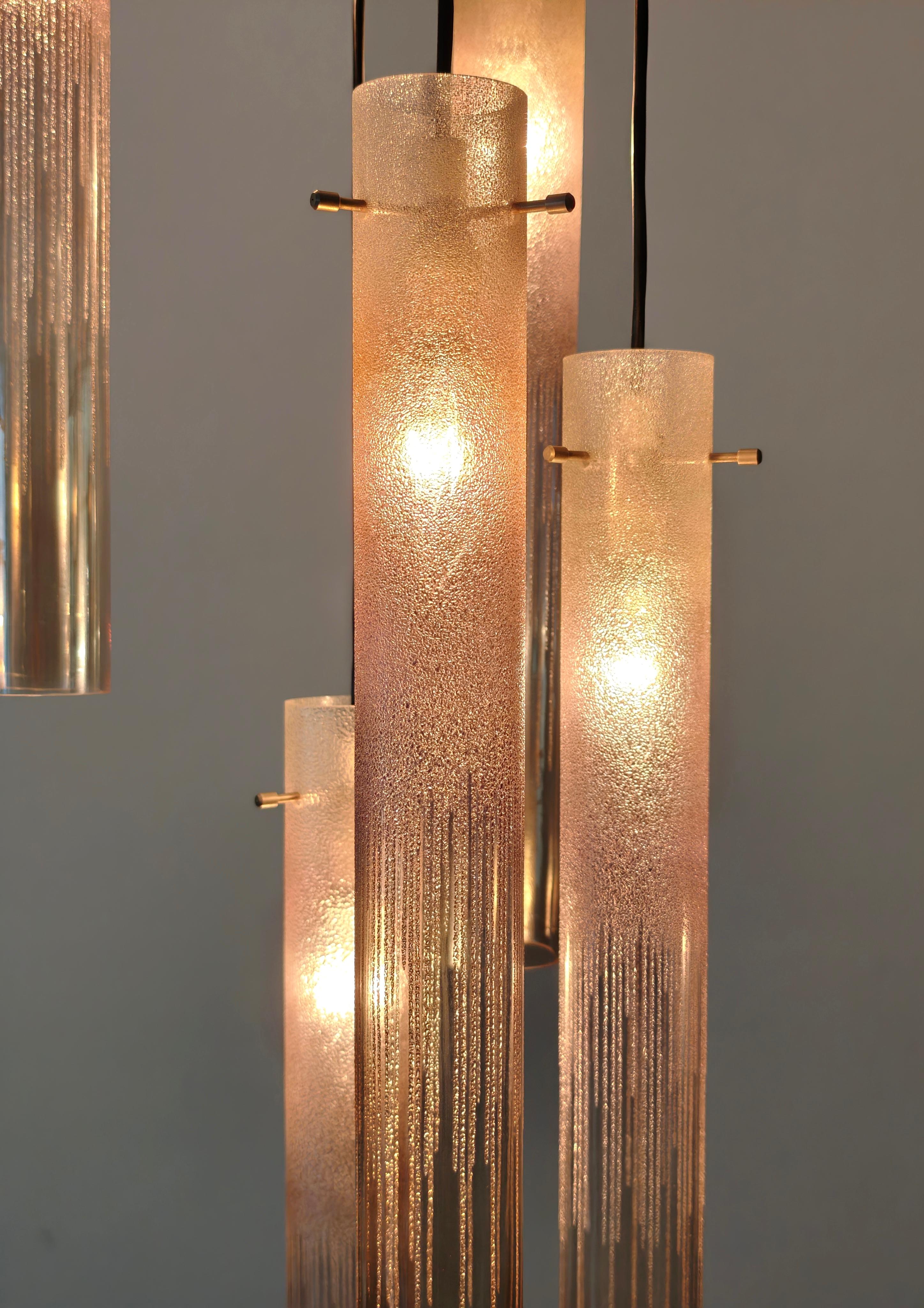 ESPERIA Fabricado en Murano, Italia, hacia 1970
Lámpara colgante de nueve luces con estructura de latón cromado cepillado y madera, difusores cilíndricos graduados de cristal ahumado y morado decorado con vetas verticales, cables eléctricos negros.
