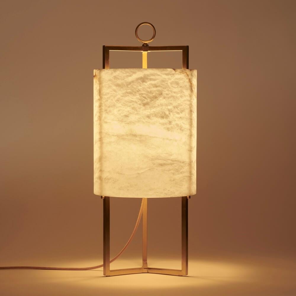 A reinterpretation of the classic lantern, where the three- stemmed brass structure supports a cylindrical lampshade made from a solid alabaster block. The evident contrast between the solidity of the stone and the lightness of the lampshade makes
