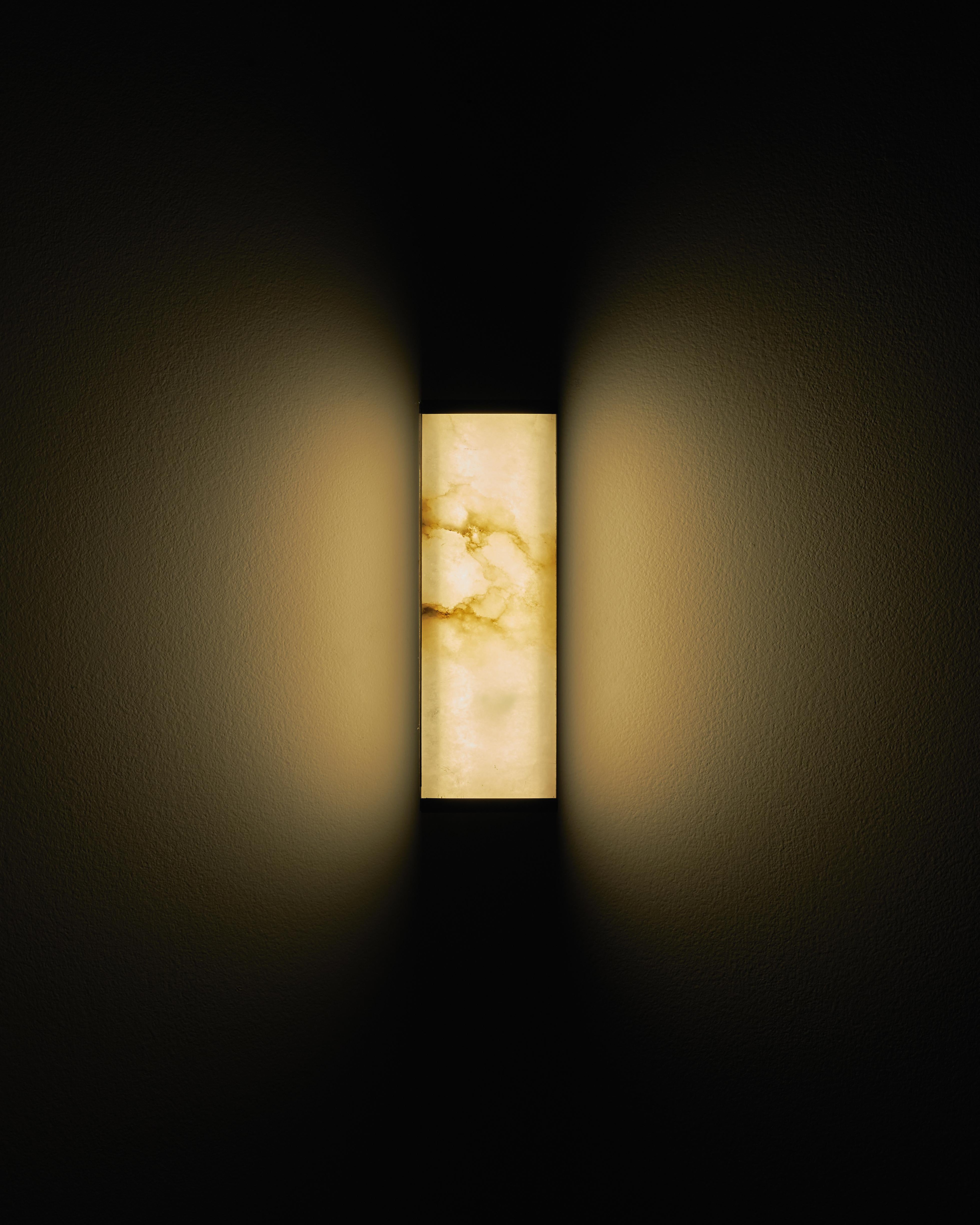 The Tech short wall sconce is a lighting fixture that was designed with the intention of merging the luminaire and lampshade into a cohesive unit, utilizing the translucent properties of ultra-thin veined alabaster to create an interplay of light