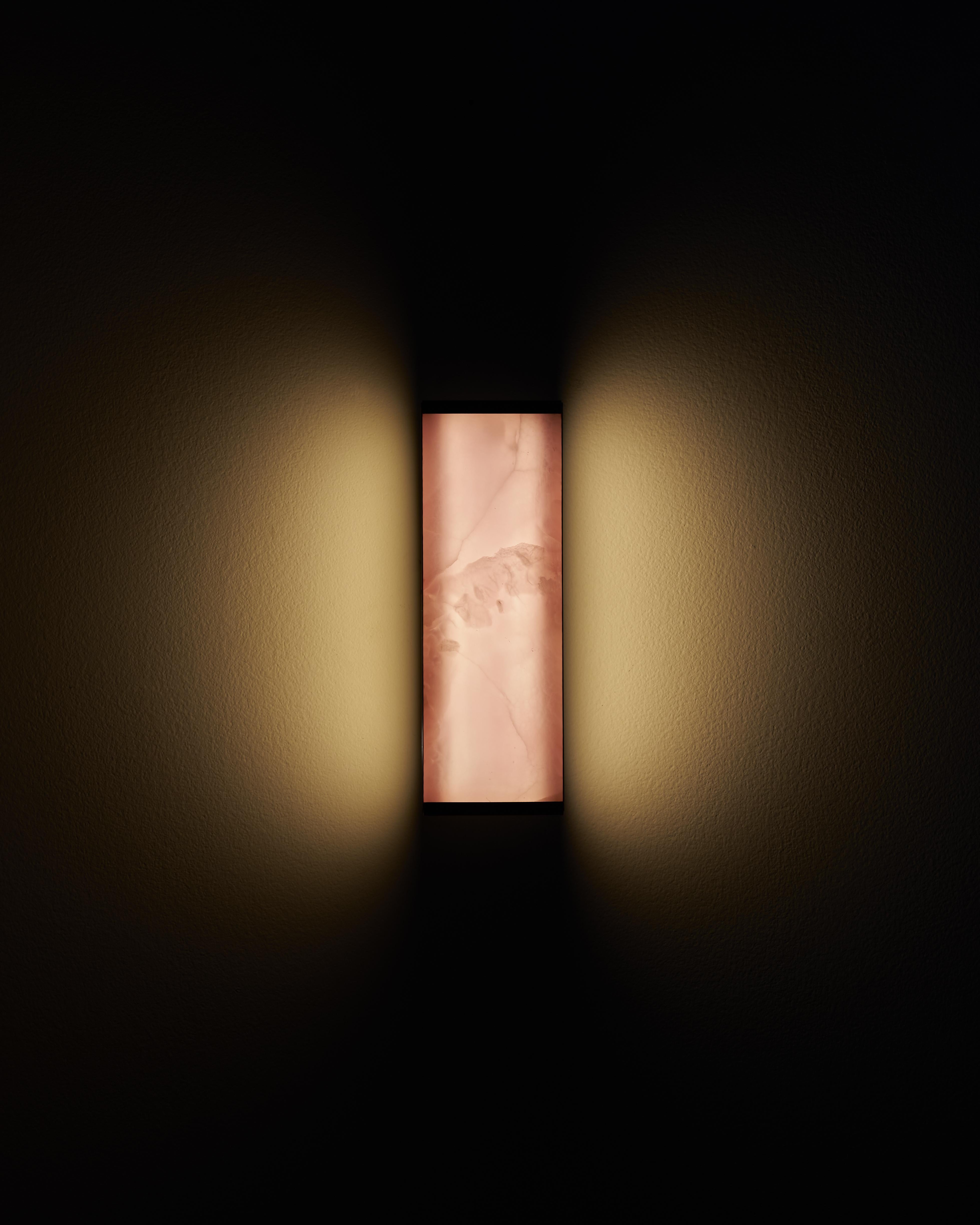 The Tech short wall sconce is a lighting fixture designed to seamlessly integrate the luminaire and lampshade into a singular unit, using the translucent properties of ultra-thin onyx to create an interplay of light and shadow that highlights the