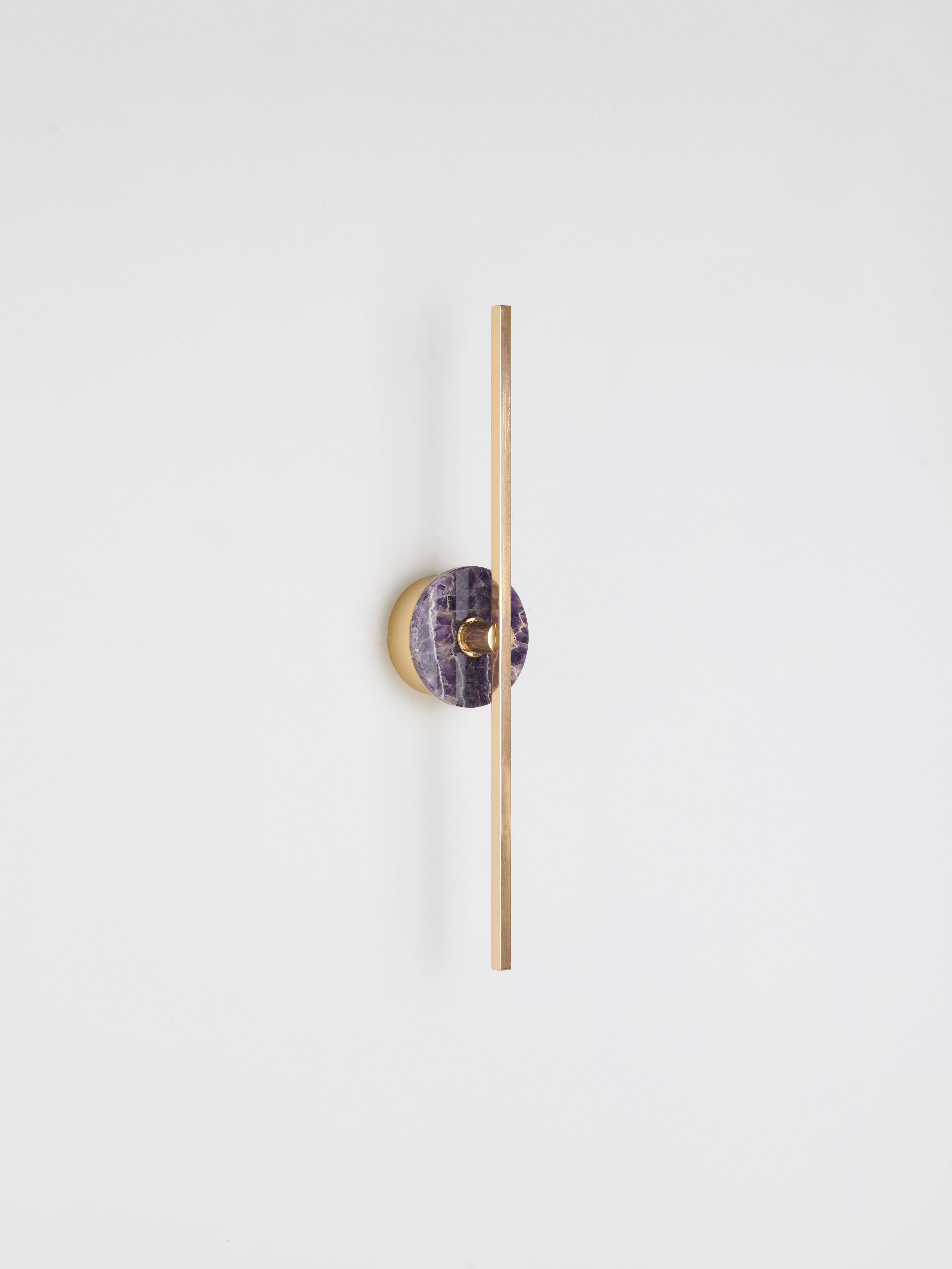 The Elite Stick wall sconce combines the minimalism of thin brass profiles with the functionality and power of led technology, offering a warm and diffused light. The amethyst, pure decorative element, embellishes the structure of the product with a