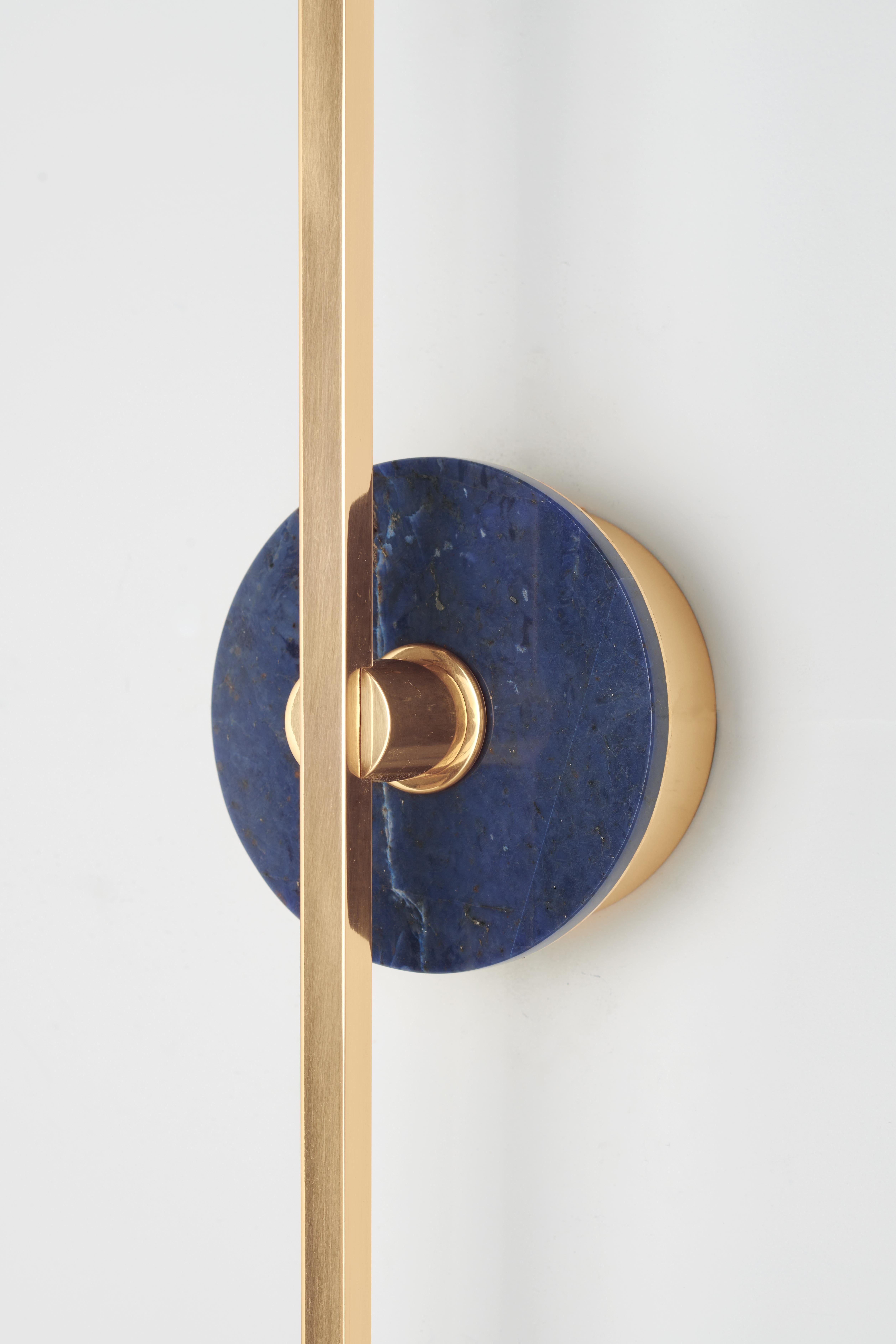 The Elite Stick wall sconce combines the minimalism of thin brass profiles with the functionality and power of led technology, offering a warm and diffused light. The sodalite, pure decorative element, embellishes the structure of the product with a
