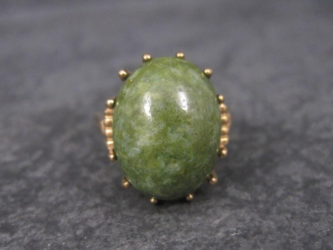 This beautiful vintage ring is solid 10k yellow gold.

It features an oval 12x16mm Jade cabochon.

The face of this ring measures 11/16ths of an inch north to south with a rise of 11mm off the finger.
This ring is a size 6.

Marks: 10K, Conjoined PA