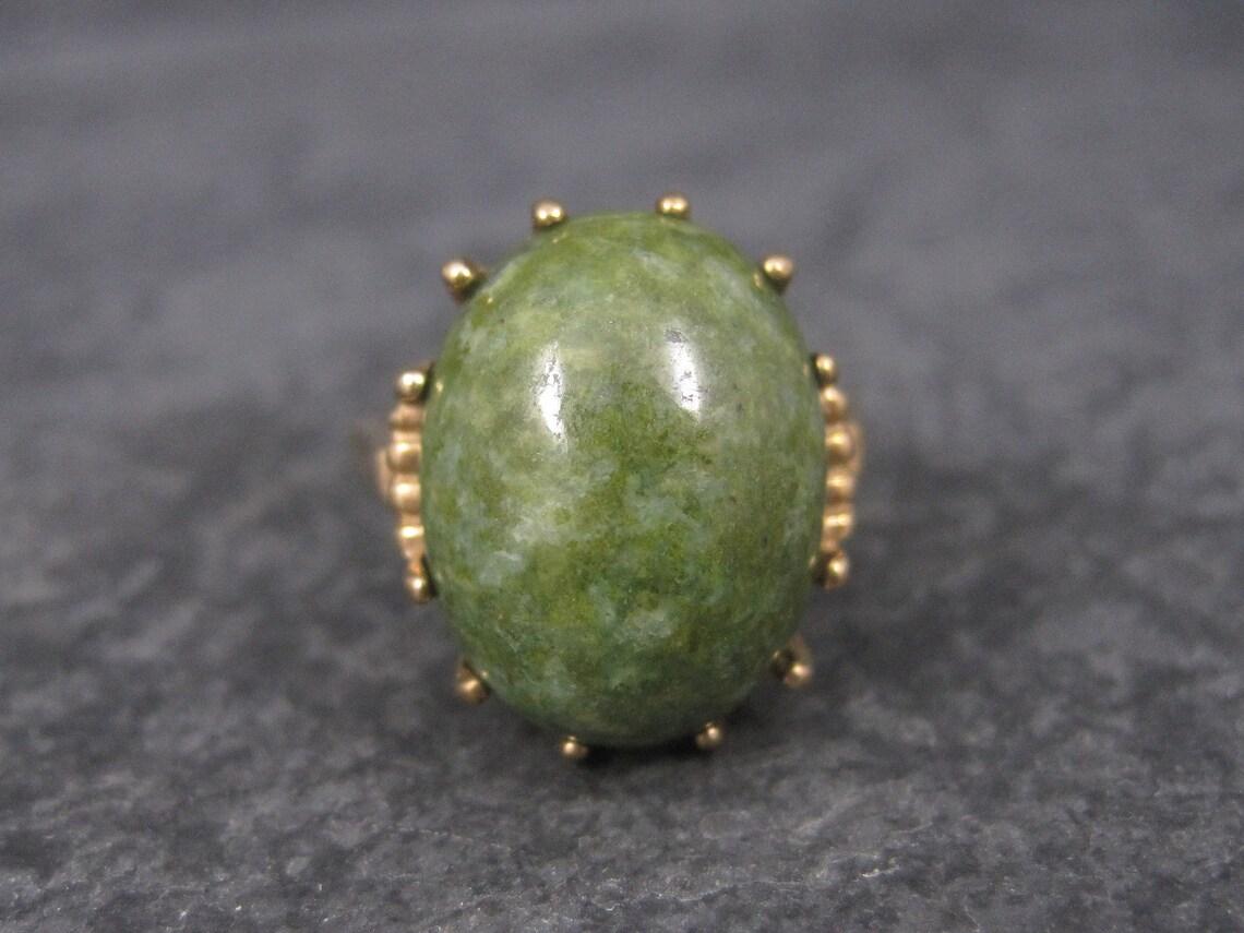 Cette magnifique bague vintage est en or jaune 10k massif.

Il est orné d'un cabochon de jade ovale de 12 x 16 mm.

La face de cette bague mesure 11/16e de pouce du nord au sud, avec une hauteur de 11 mm par rapport au doigt.
Cette bague est de