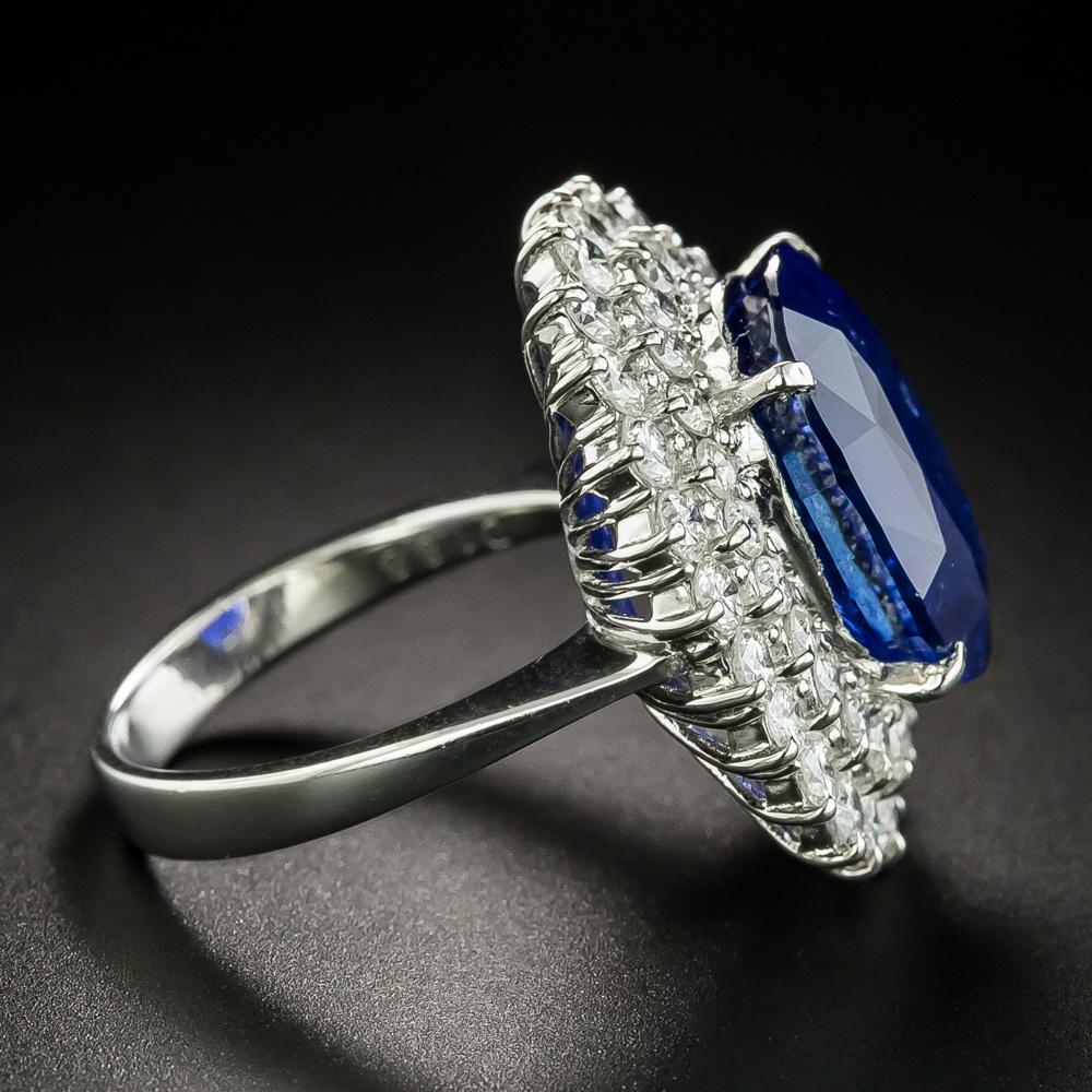 A stunning and impressively proportioned gemstone, a 12.18 carat faceted oval sapphire of Ceylon (Sri Lanka) origin, radiates a gorgeous rich royal blue hue from within a double halo composed of sparkling bright white round brilliant-cut diamonds in