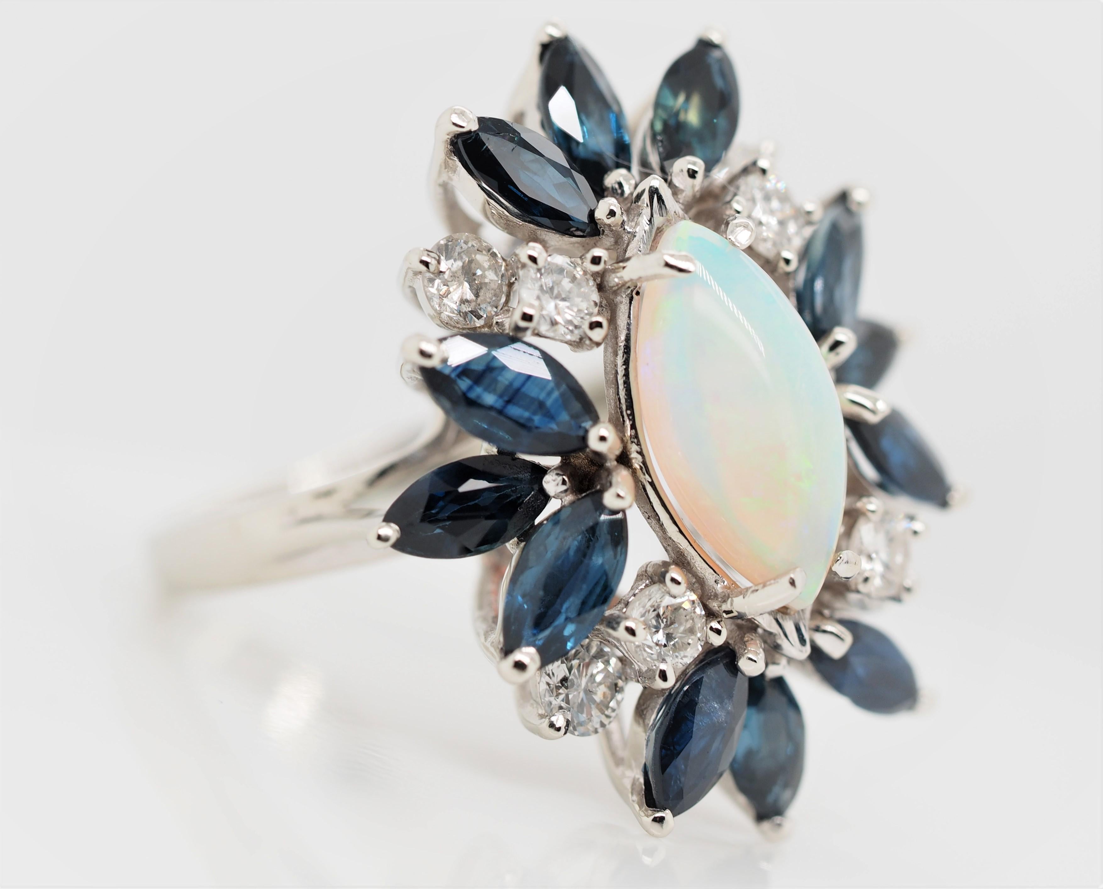 Bague cocktail en or blanc 14K avec opale, saphir et diamant.  La bague présente une belle opale marquise, entourée d'un halo ondulant de saphirs marquises et de diamants pleine taille. La pierre est sertie dans une monture à quatre griffes en or