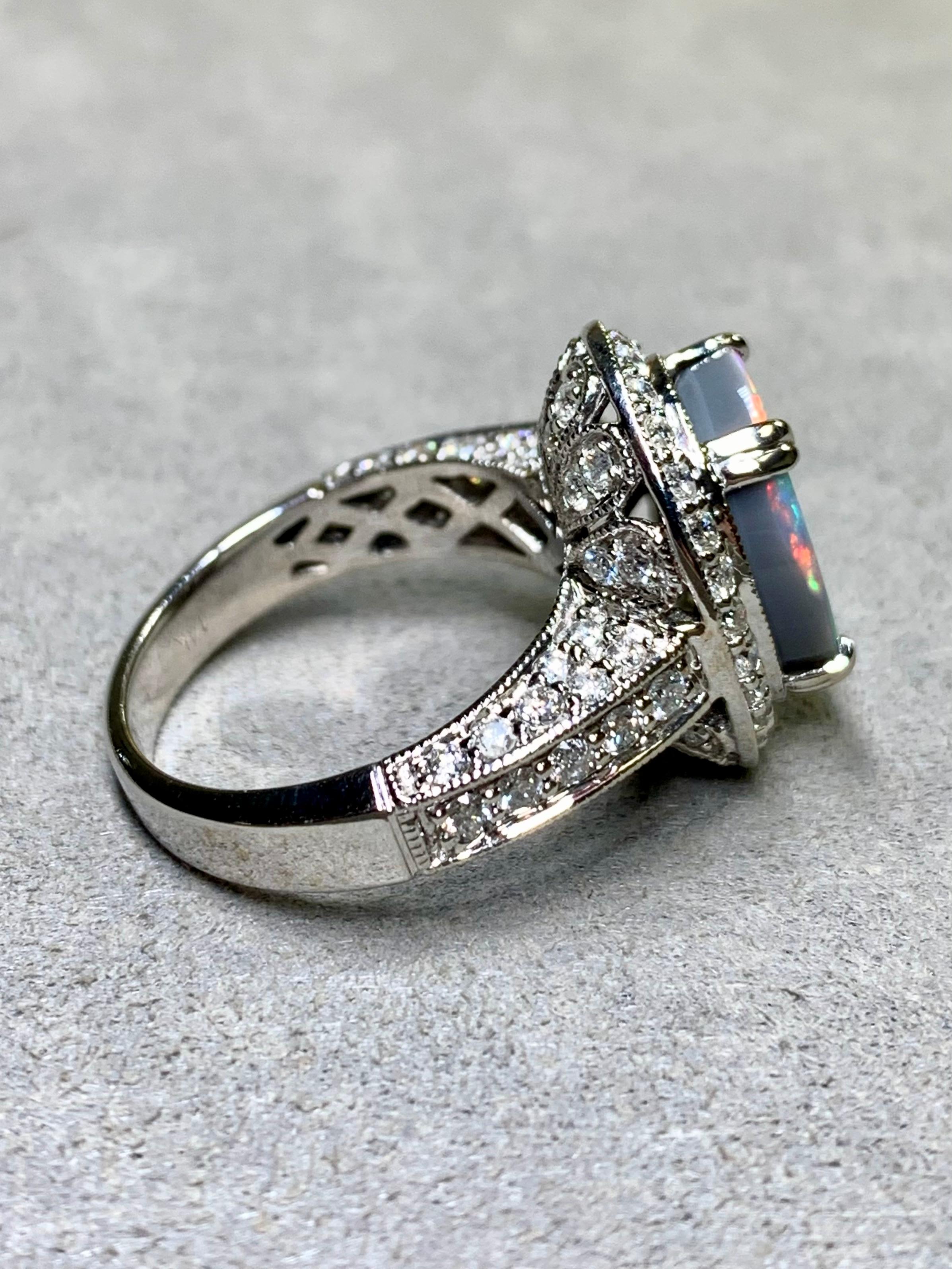 
Un classico anello da cocktail a forma di aureola in oro bianco 14K, centrato da un opale nero naturale da 3,44 carati (pesato) con splendidi colori arancioni, rossi, gialli e verdi. La pietra centrale è circondata da circa 1,42 carati di diamanti