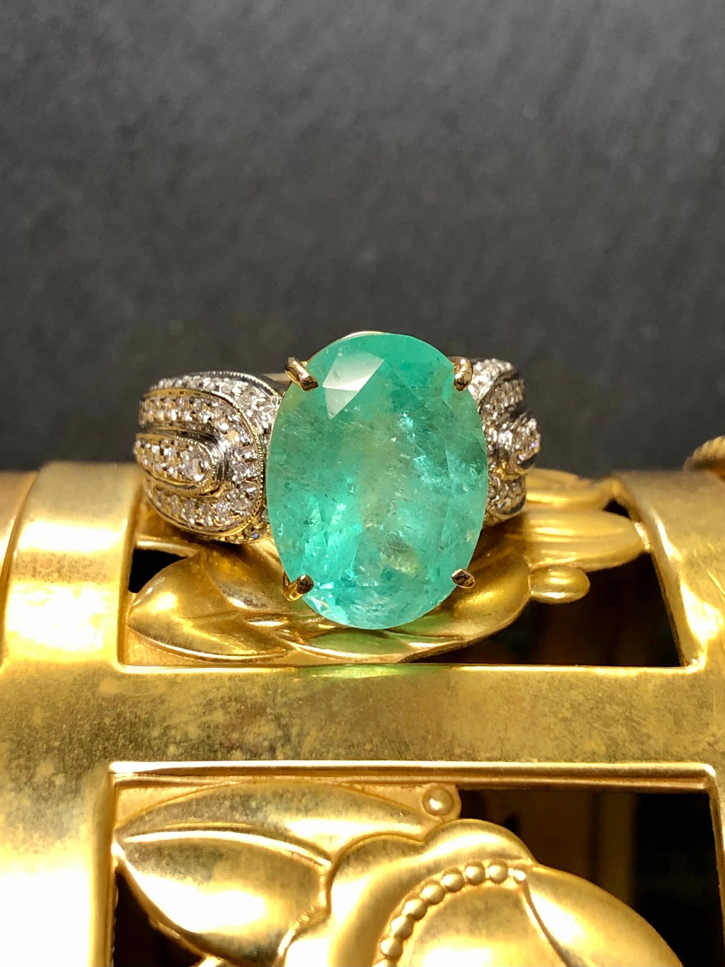 An impressive cocktail ring done in 14K white gold and yellow gold centered by an approximately 8.34ct oval cut natural emerald (15.11mm x 11.27mm x 8.82mm). The center stone is flanked by approximately .90cttw in round cut diamonds averaging H-I in