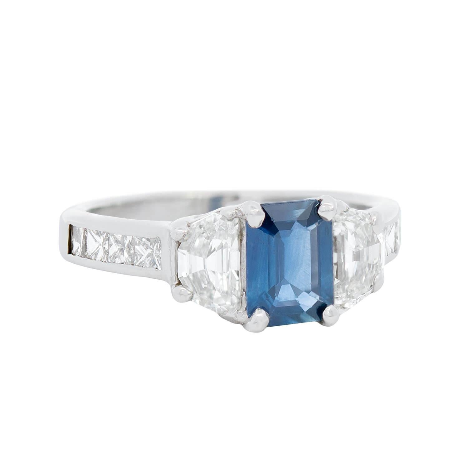 Une magnifique bague en saphir et diamant de style Estate ! Cette magnifique pièce est fabriquée en or blanc 14k et présente un saphir émeraude de 0,85ct serti au centre. Le saphir est encadré par deux diamants de taille Cadillac sertis à