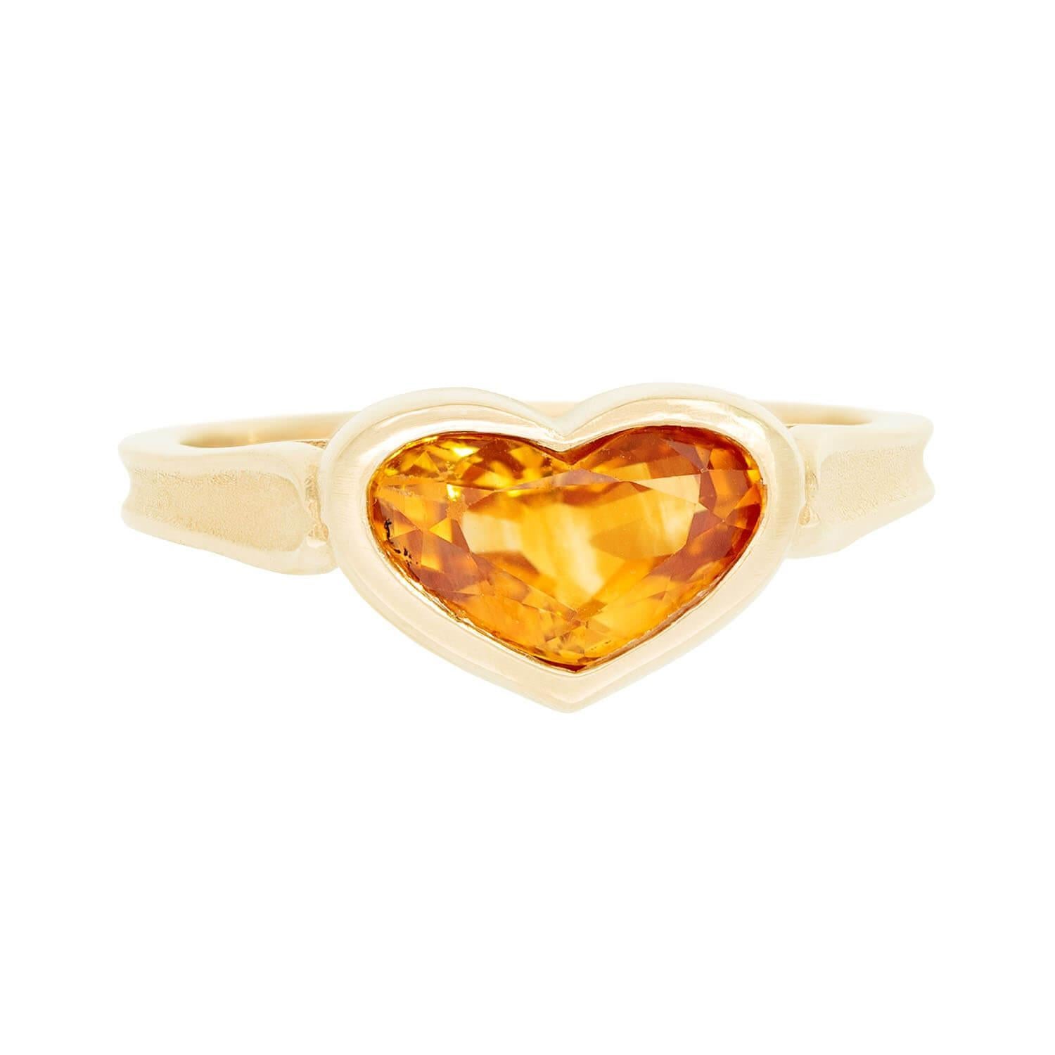 A beautiful yellow sapphire ring! Crafted in 14k yellow gold, this wonderful piece forms the shape of a small heart, which features a central heart cut yellow sapphire stone. The bezel set sapphire displays a stunning rich yellow tone, which