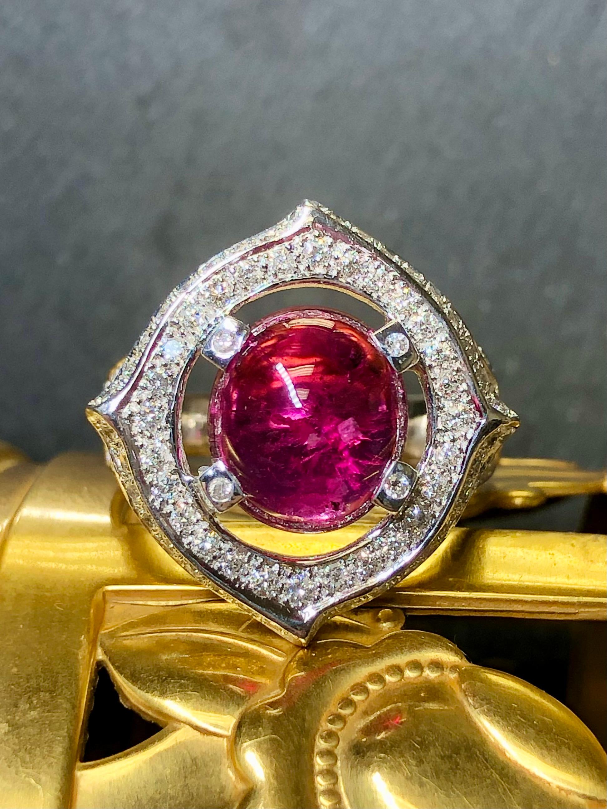 An eye catching and lively ring with a beautiful pop of color. This piece is crafted in 14k white gold and centered by an approximately 6.70ct natural cabochon cut pink tourmaline surrounded by 1.10cttw in G-I color Vs2-Si2 clarity round