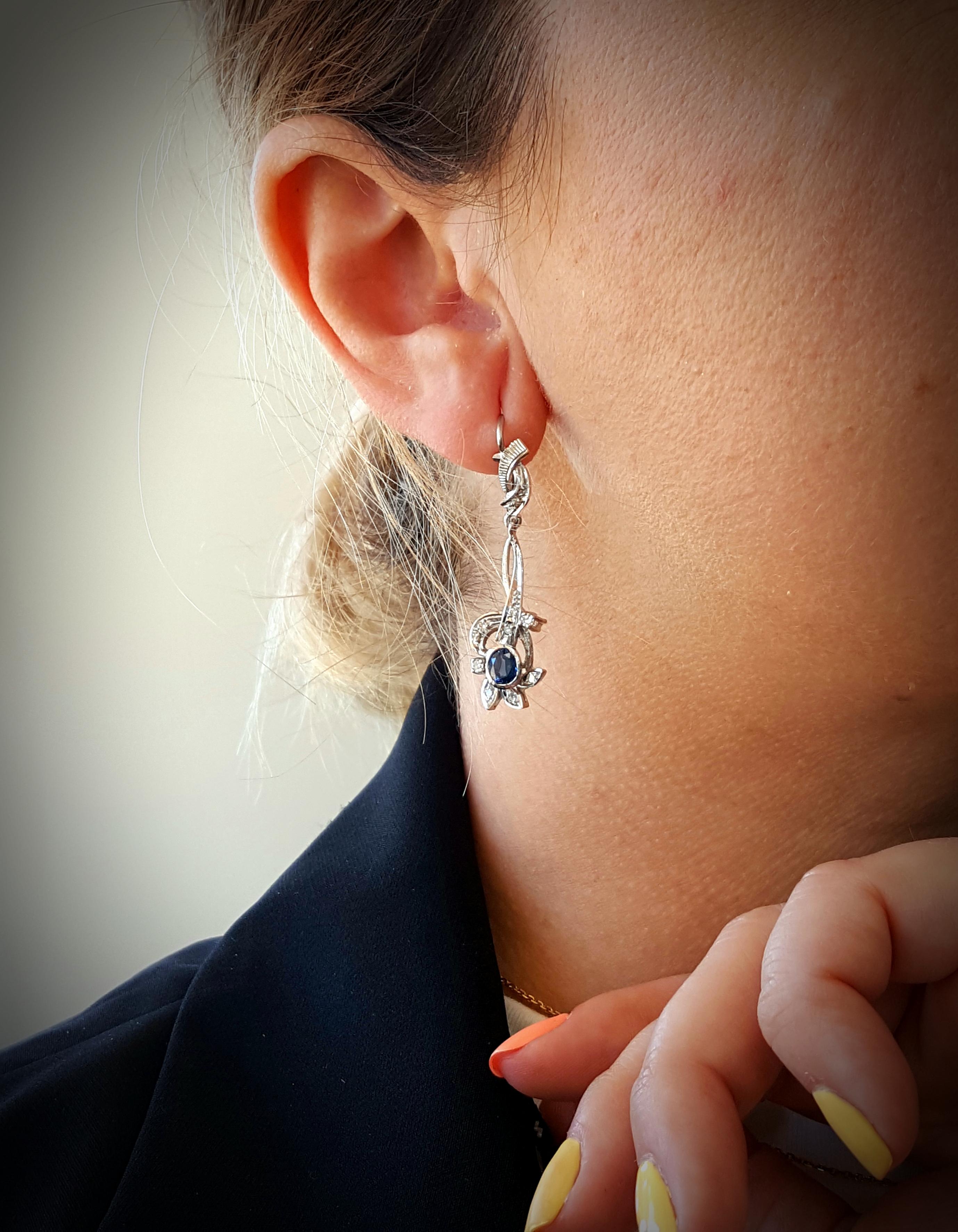 Estate 14 Karat White Gold Blue Sapphire and Diamond Leverback Earrings.  The earrings feature a pair of beautifully matched oval shaped blue sapphires.  The stones are each set into a 14 karat white gold bezel enhanced by an ornate pattern of