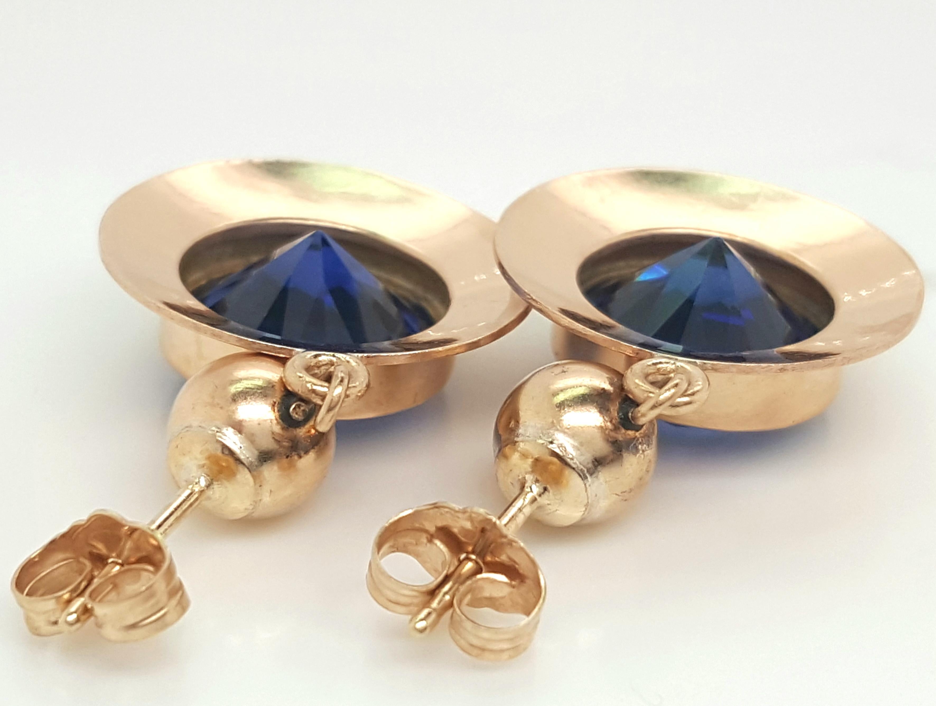 Estate 14 Karat Yellow Gold Synthetic Sapphire Dangle Earrings.  The earrings feature a pair of impressively sized round blue synthetic sapphires.  The stones are each set into a 14 karat yellow gold bezel enhanced by a recessed textured gold halo,