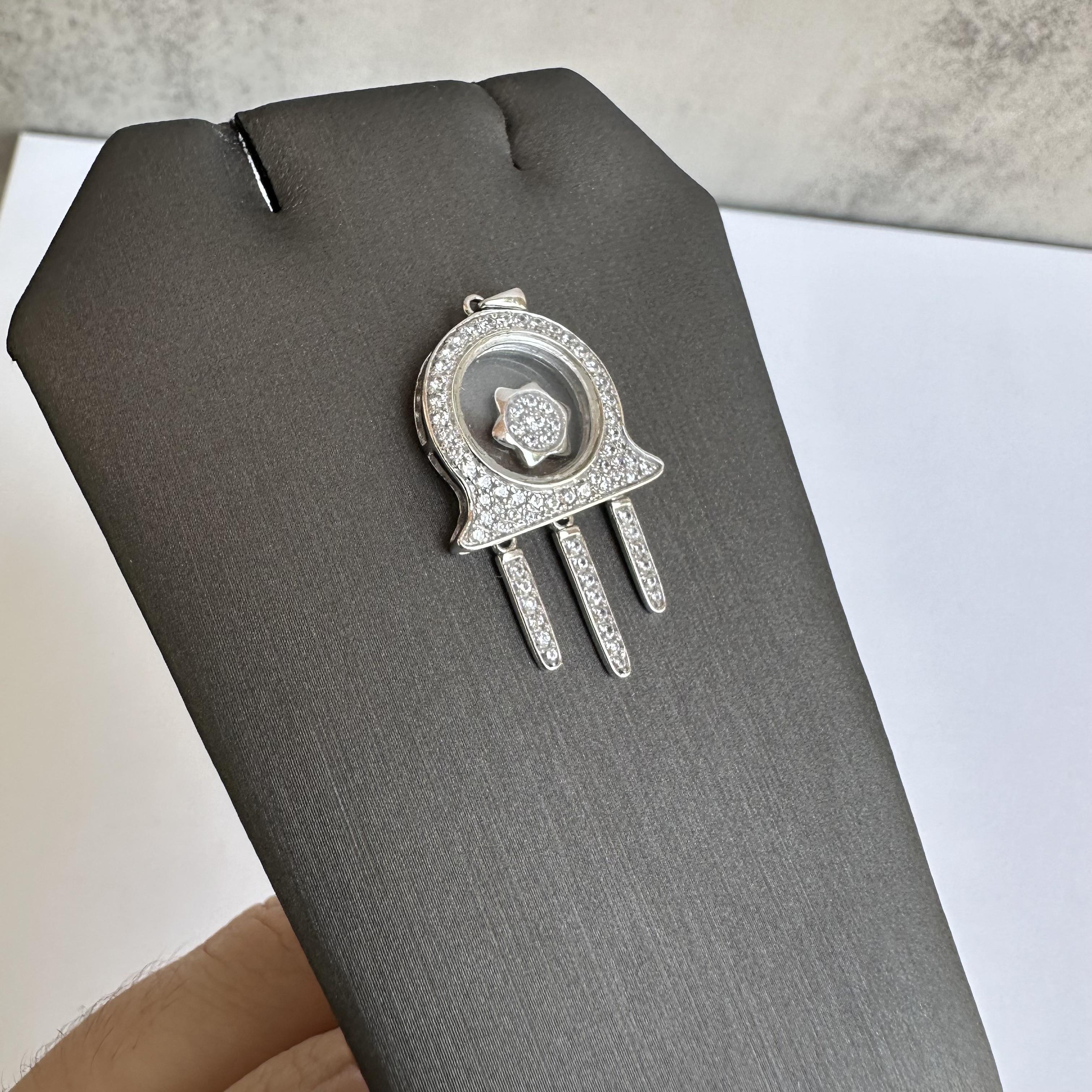 Add a meaningful and stylish piece to your jewelry collection with this 14kt White Gold Moving Hamsa Pendant. Weighing 3.63 grams and adorned with glass/CZ stones, this pendant beautifully captures the symbolic Hamsa design, known for its protective