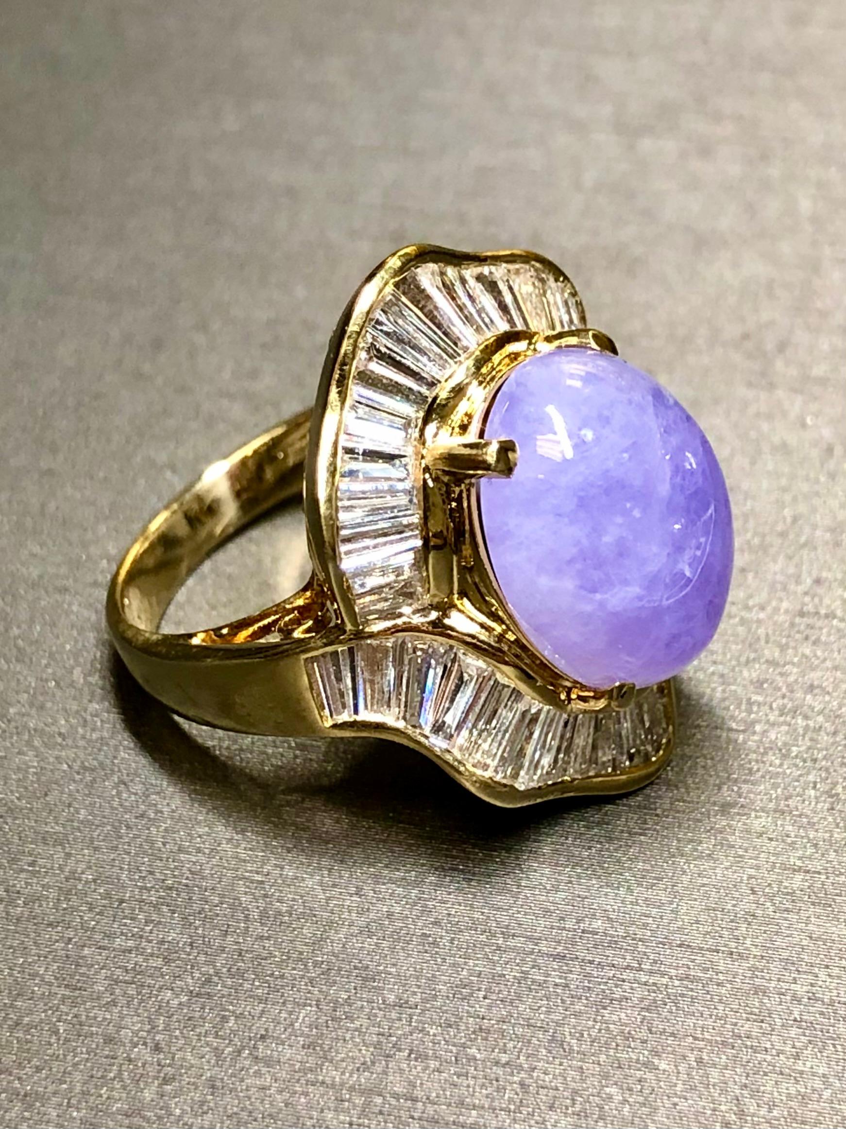 An absolutely spectacular cocktail ring crafted in 18K yellow, gold and centered by a 9.03ct natural lavender jade cabochon surrounded by approximately 3.80cttw in G-H color Vs1-2 clarity straight and tapered, baguette diamonds. The setting is just