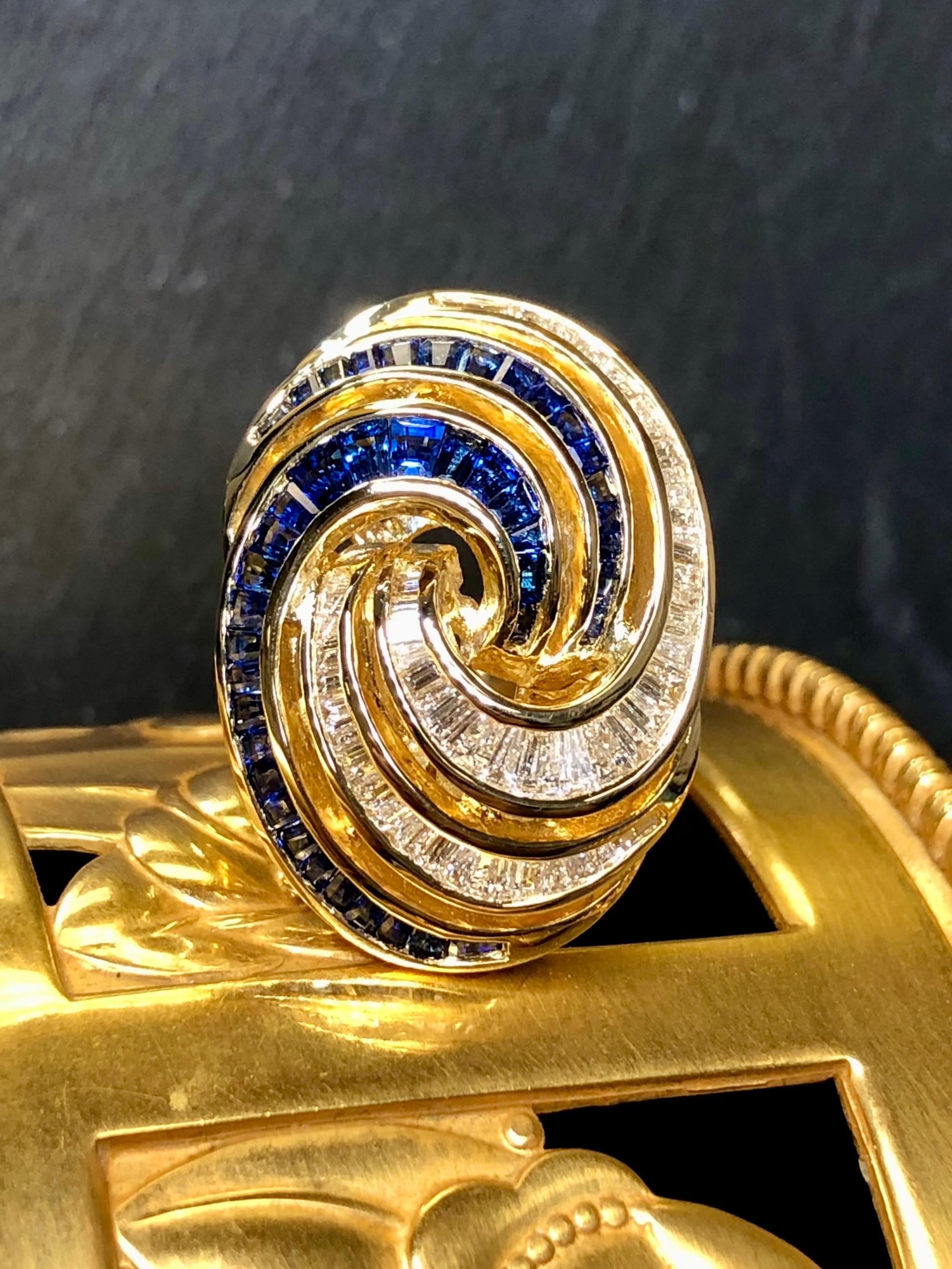 Une bague de cocktail fantaisiste et à la pointe de la mode, réalisée en or jaune 18 carats et sertie d'environ 3cttw de saphirs baguettes bleu vif ainsi que de 2,10cttw de diamants baguettes de couleur H-I et de pureté Vs1-2.


Dimensions/Poids