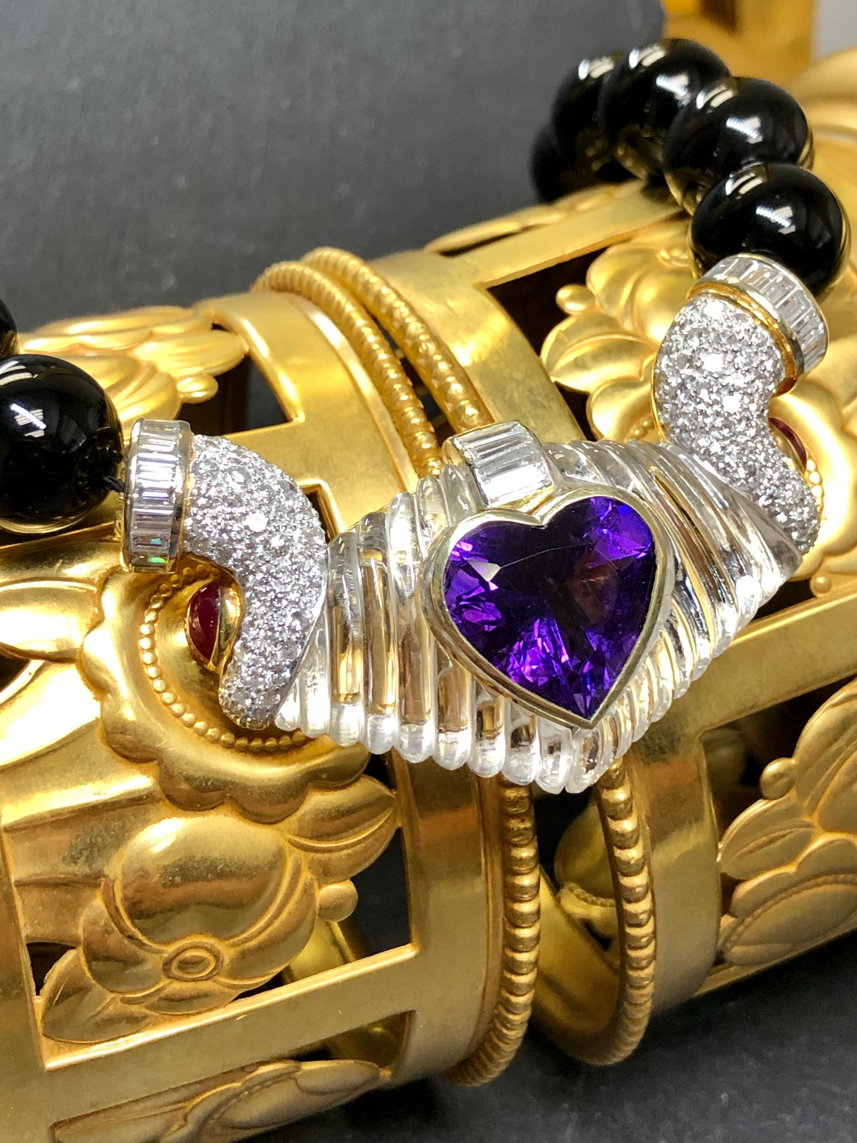 
A one-of-kind necklace done in 18K gold and pave set with approximately 4.80cttw in F-G color Vs1-2 round and baguette diamonds. The central portion is natural carved rock crystal quartz bezel set with a central heart shaped natural amethyst