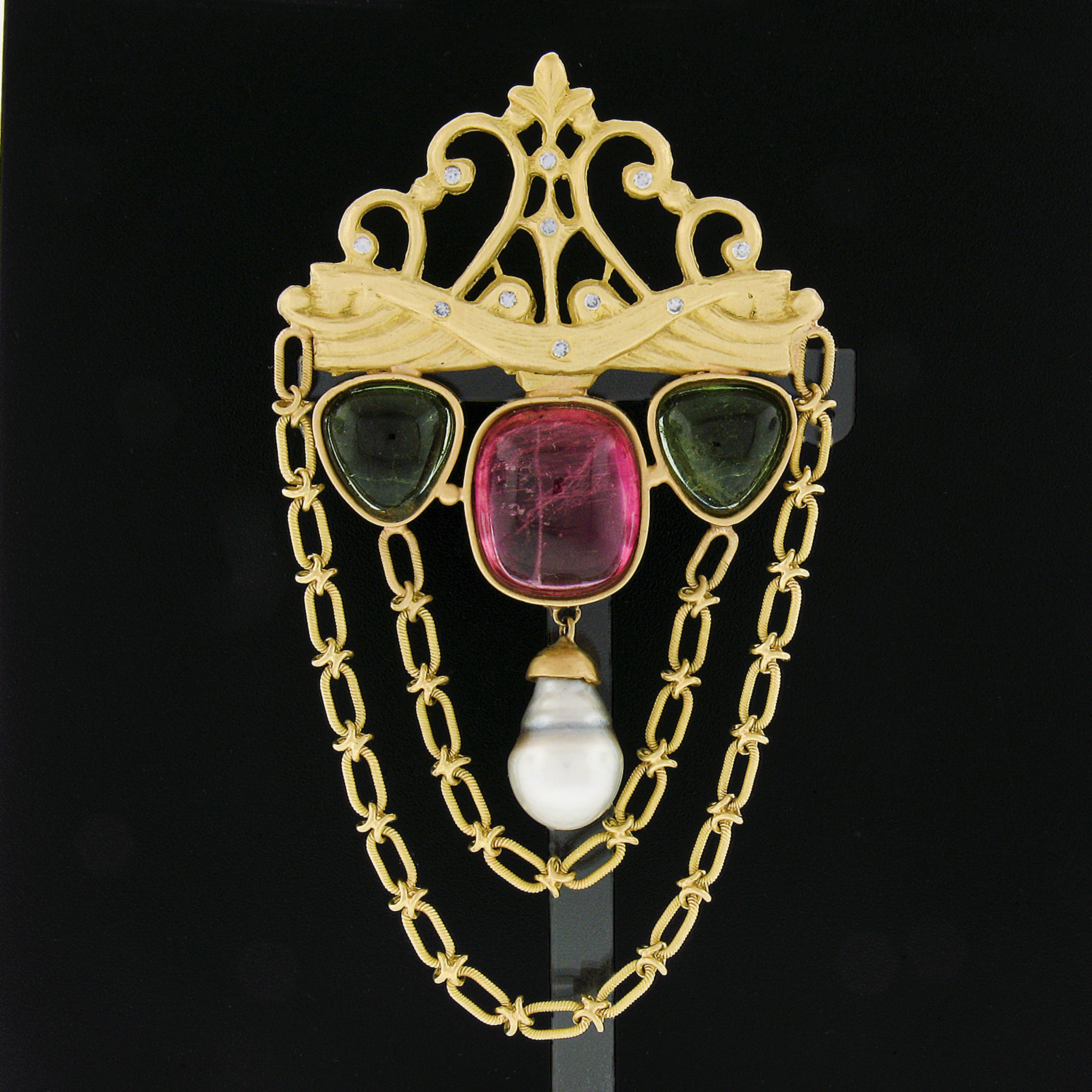 This substantial and uniquely designed pin brooch is crafted in solid 18k yellow gold and features a wonderfully detailed design adorned with cabochon cut pink and green tourmaline stones that are large and rich in color. Two well made link chains