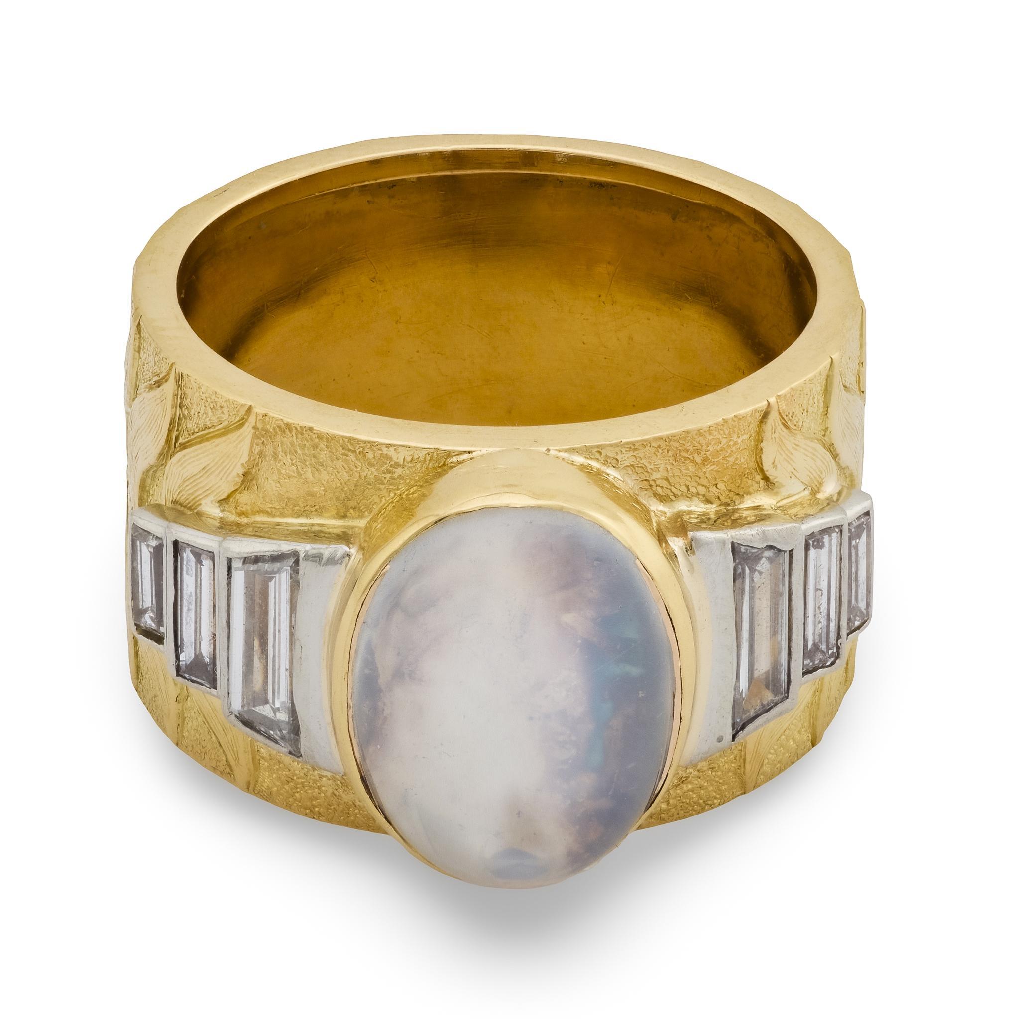 A fabulous moonstone cigar band! Crafted in vibrant 18k yellow gold, this piece features a central, bezel-set moonstone cabochon. The oval-cut moonstone displays a lovely grayish-blue hue, and is bordered on both the left and right by 3 baguette-cut