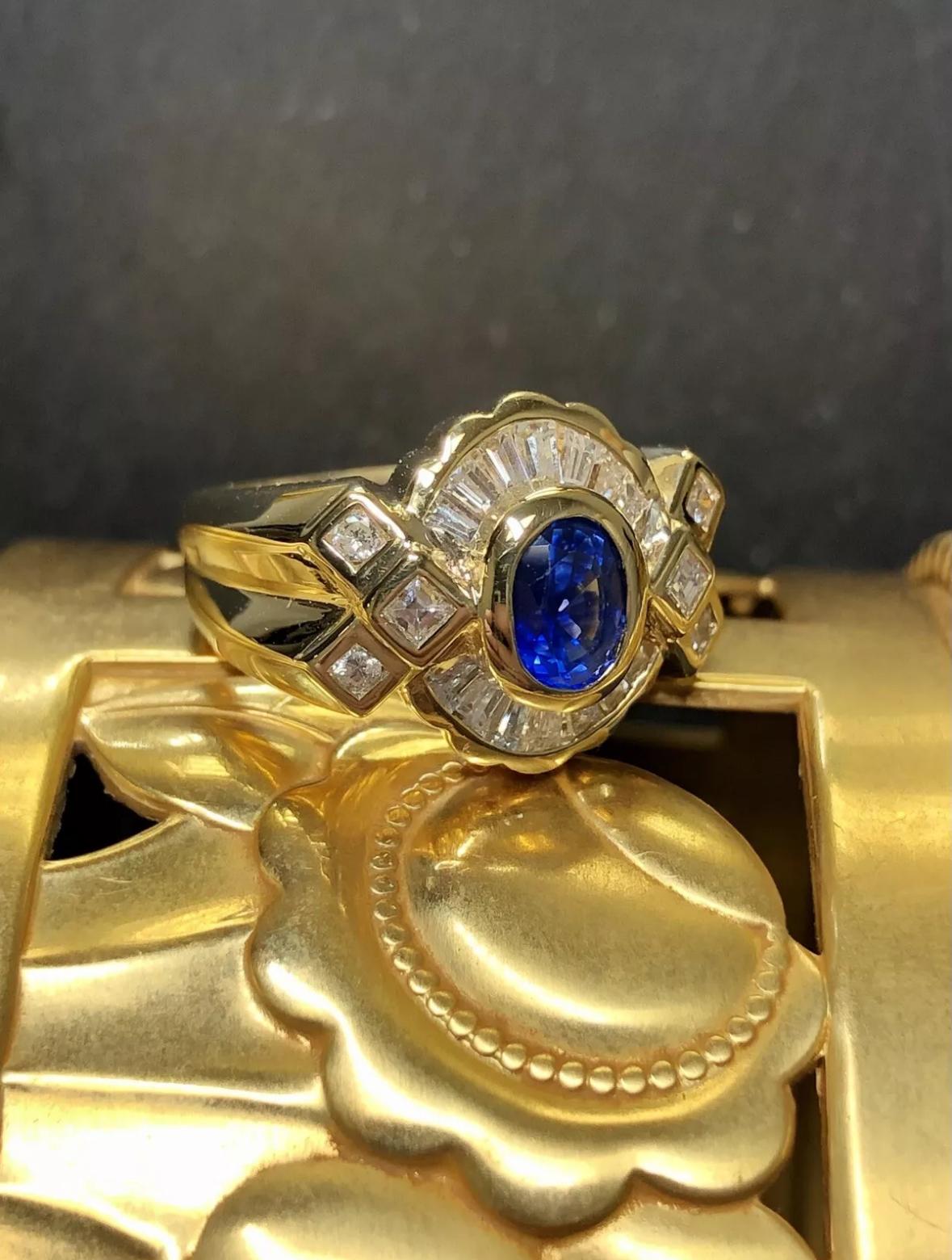 A gorgeous ring done in supple 18K yellow gold and centered with a stunning royal blue natural bezel set sapphire weighing approximately .80ct surrounded by approximately 1.60cttw in tapered and square baguette as well as round
