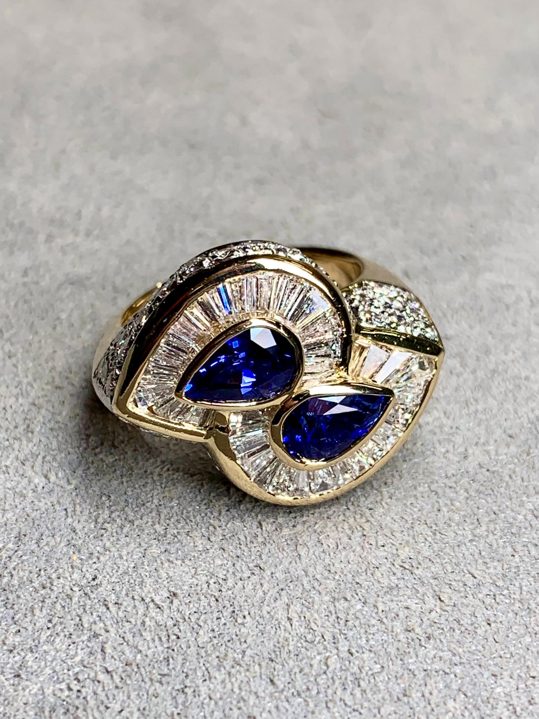 A bright and lively cocktail ring done in 18K yellow gold and centered by two pear shape natural blue sapphires weighing approximately 1ct each (2ctw) surrounded by approximately 3.23ctw in tapered baguette and round diamonds ranging G-I in color