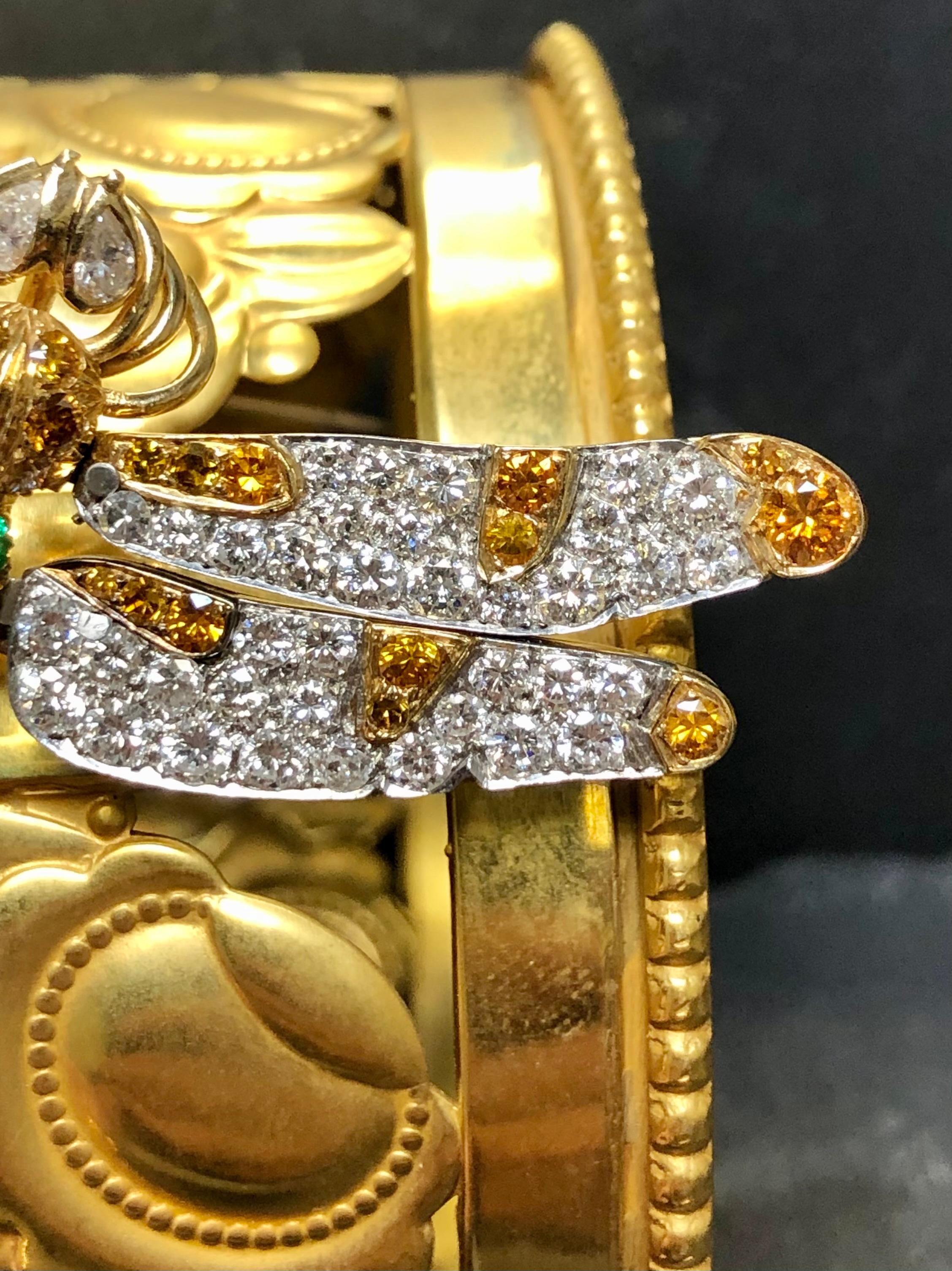 Une broche libellule magnifiquement détaillée réalisée en or jaune 18K et en platine, sertie d'environ 4cttw de diamants blancs de couleur G-H et de pureté Vs ainsi que d'environ 1cttw de diamants orange et de nombreuses émeraudes naturelles.