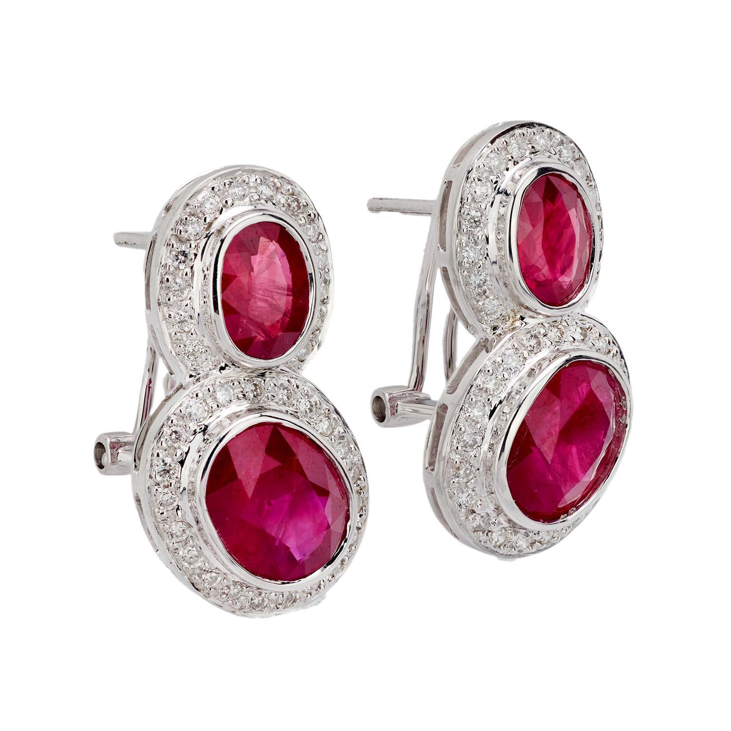 An exquisite pair of ruby and diamond earrings! Crafted in 18k white gold, each earring features two oval-cut rubies, which are held within bezel settings. Each pinkish-red ruby is bordered by a halo of modern round brilliant cut diamonds, which are