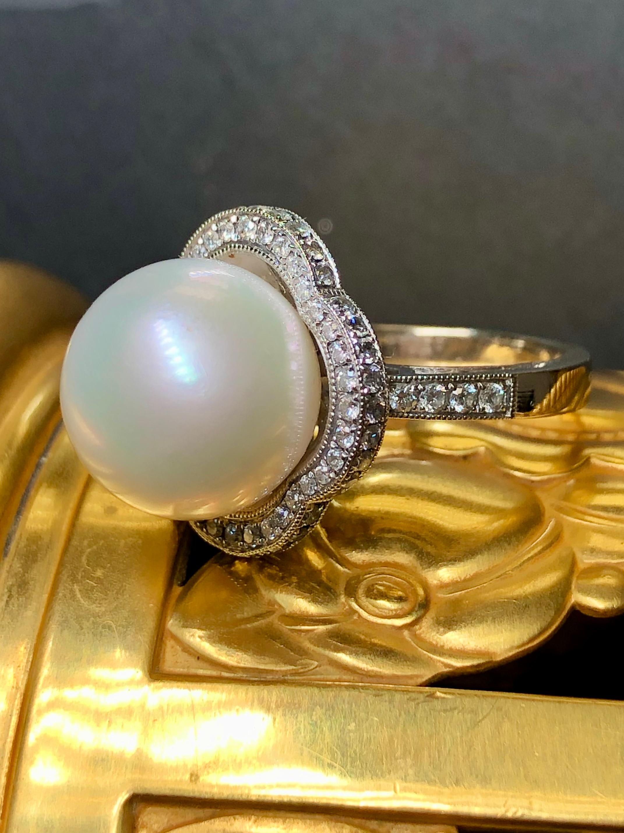 An elegant and timeless ring done in 18K white gold centered by a cream colored 13.4mm large South Sea pearl with very minor pitting and a beautiful, even luster. Bead set around the pearl and on the shoulders of the ring is .73cttw in perfectly