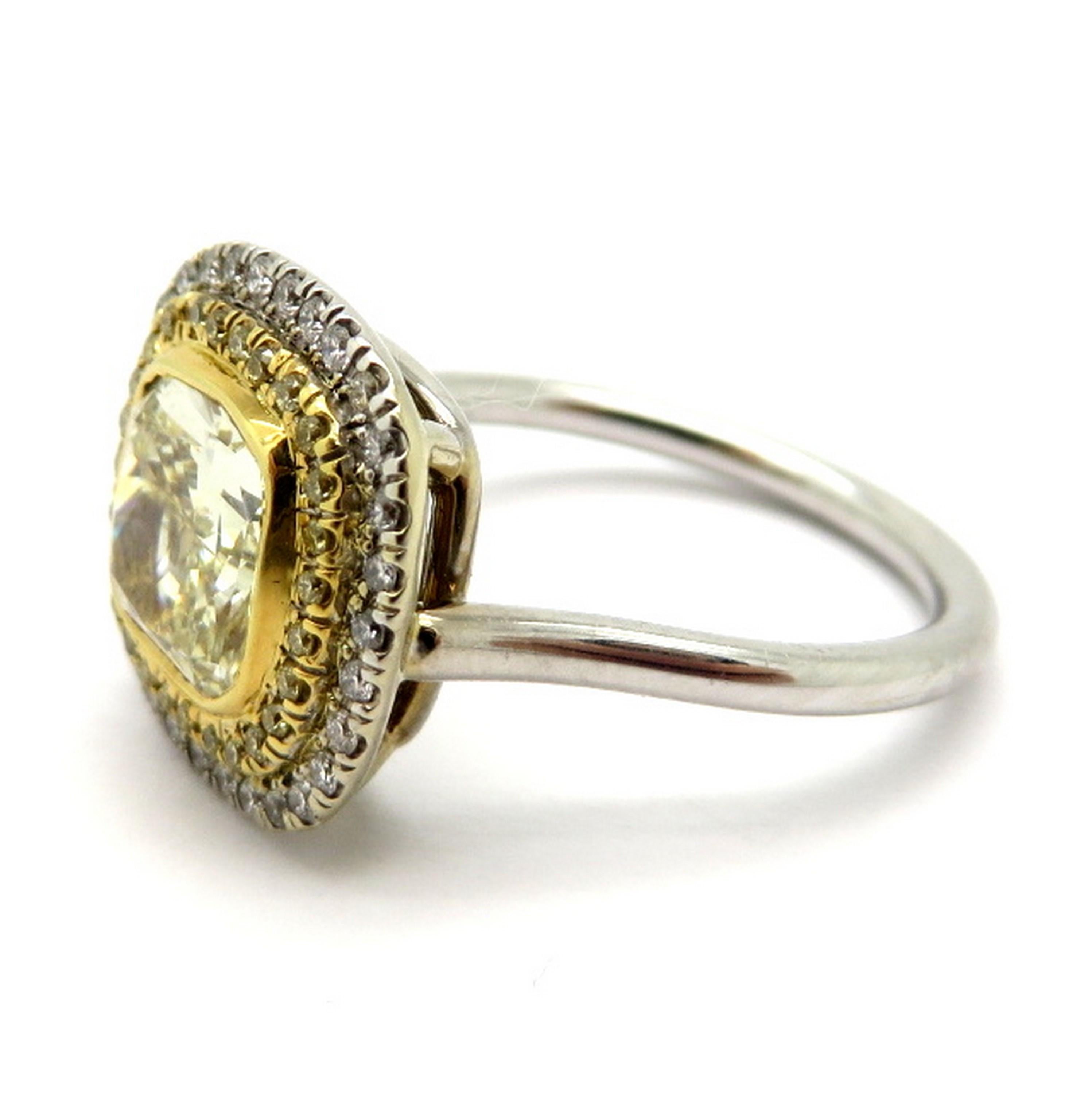 Estate 18K two-tone yellow radiant cut diamond halo engagement ring. Showcasing one fancy light yellow radiant cut diamond, bezel set, having VS1 clarity grade, weighing approximately 2.08 carats. Accented with 27 fancy yellow round brilliant cut