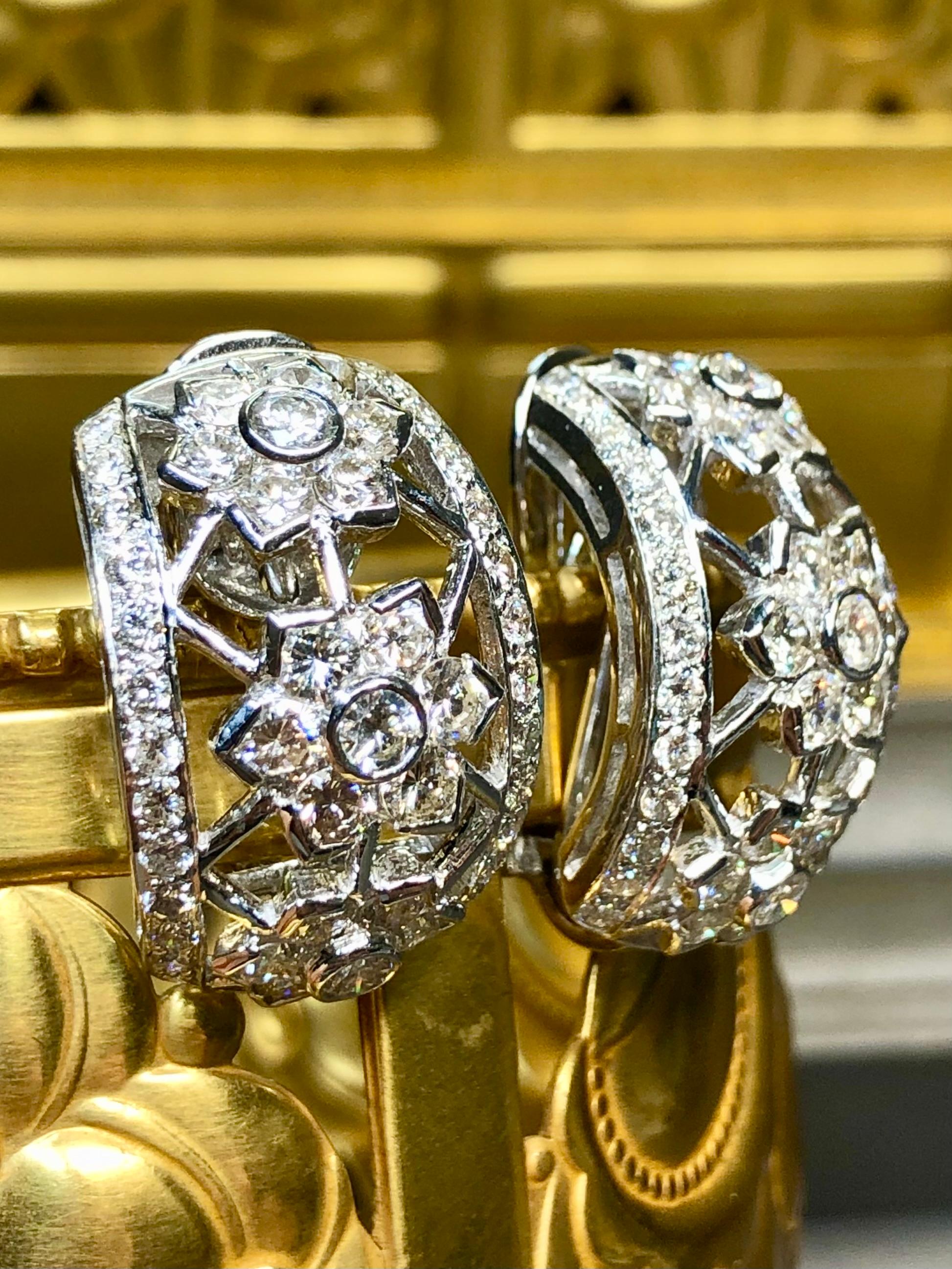 A classic pair of curved “shrimp” huggie earrings done in 18K white gold in an open work floral design. They are bezel and bead set with approximately 4.65cttw in H-J color Vs1-2 round diamonds. These earrings have swing posts with omega