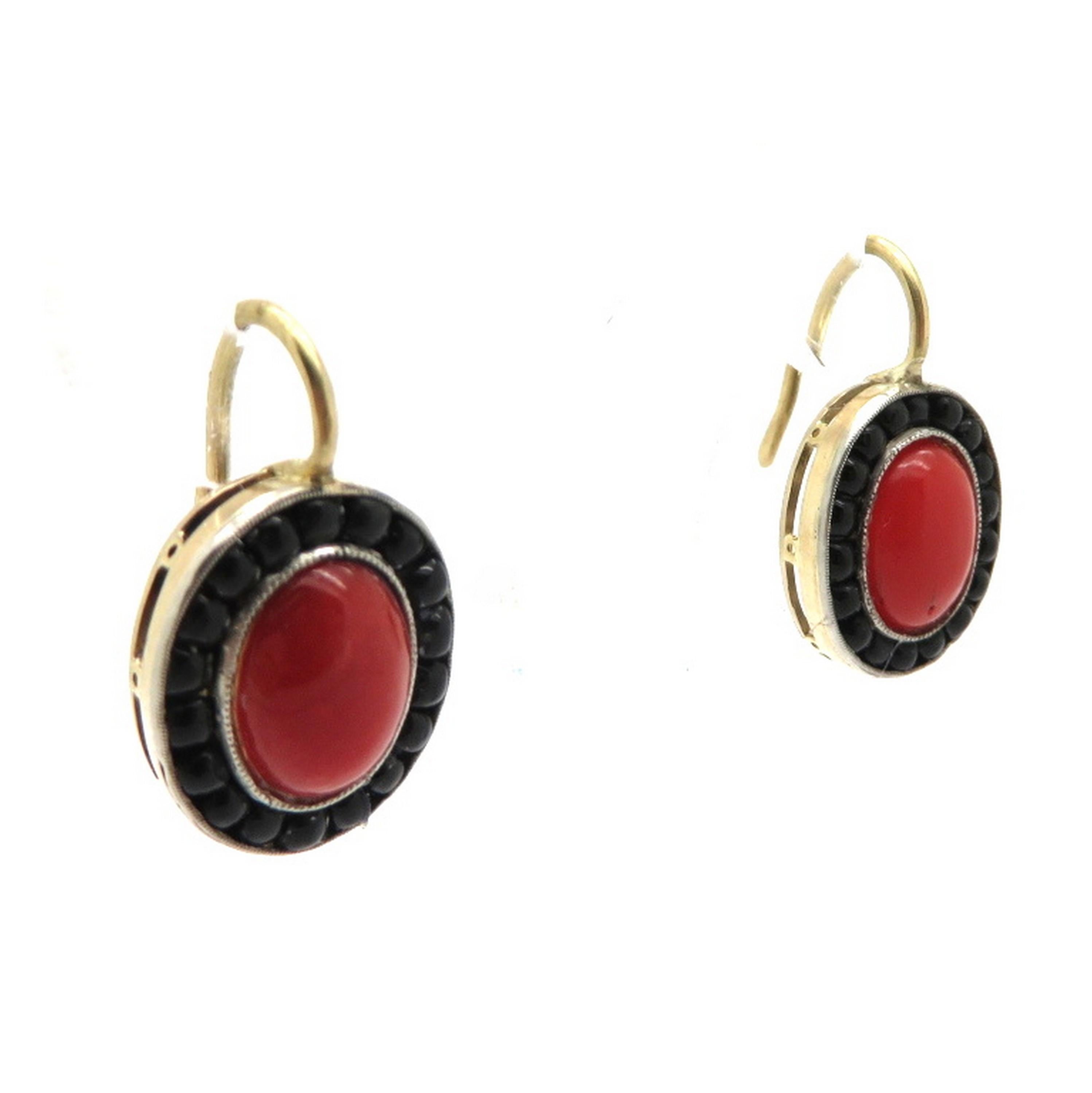 Estate 18K yellow gold 1950s coral and onyx dangle earrings. Centering two red coral cabochons. Each earring is accented with a halo with a total of 36 round cabochon black onyx channel set beads. The earrings are crafted out of 18K yellow gold and
