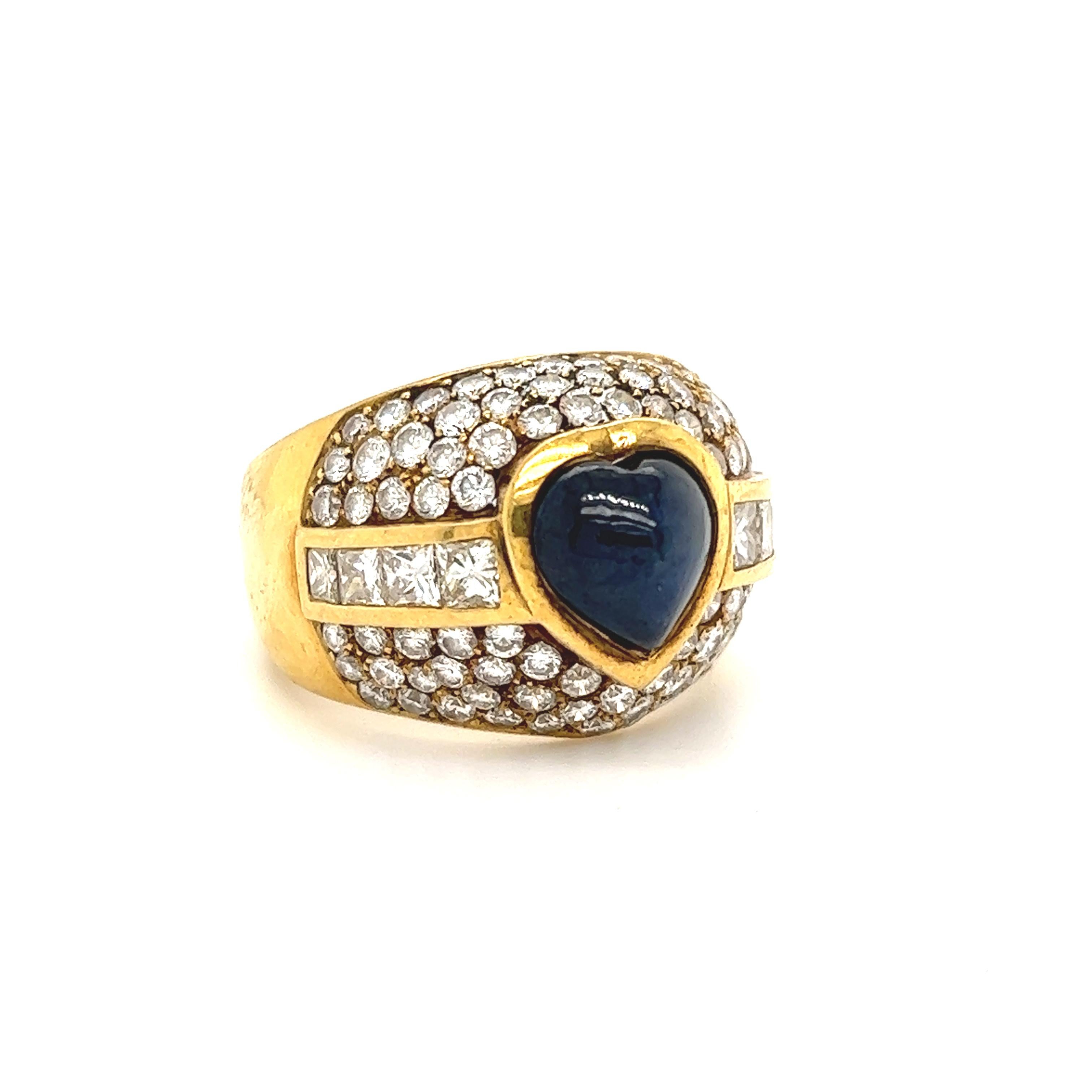 Exceptional design seen on this 18k yellow gold ring. The highlight of the ring is one heart shaped blue sapphire that is bezel set in the center of the ring. The sapphire shows a rich blue color that stands out against the yellow gold and diamond