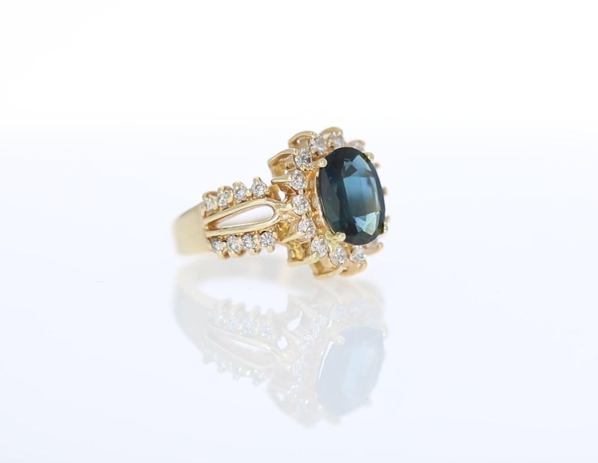 This 14 K yellow gold estate ring is centered by an oval grayish-blue sapphire weighing approximately 2.50 carats.  A halo of round diamonds surround the sapphire and provide accents partially on the shank.  The diamonds weigh approximately 0.50